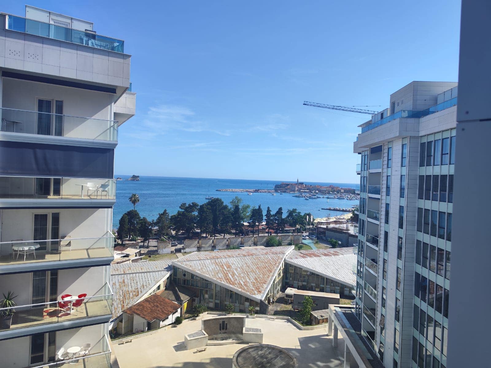 View from the balcony of a modern apartment in Budva, Montenegro: a panorama of the Adriatic Sea, the beach, and the cityscape.