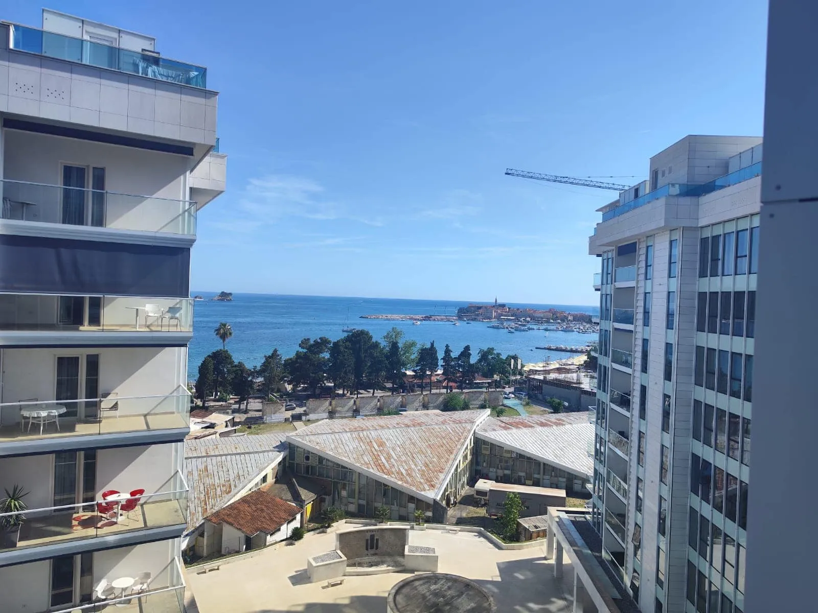 View from a balcony showing the sea, neighboring buildings with terraces, and rooftops on a sunny day.