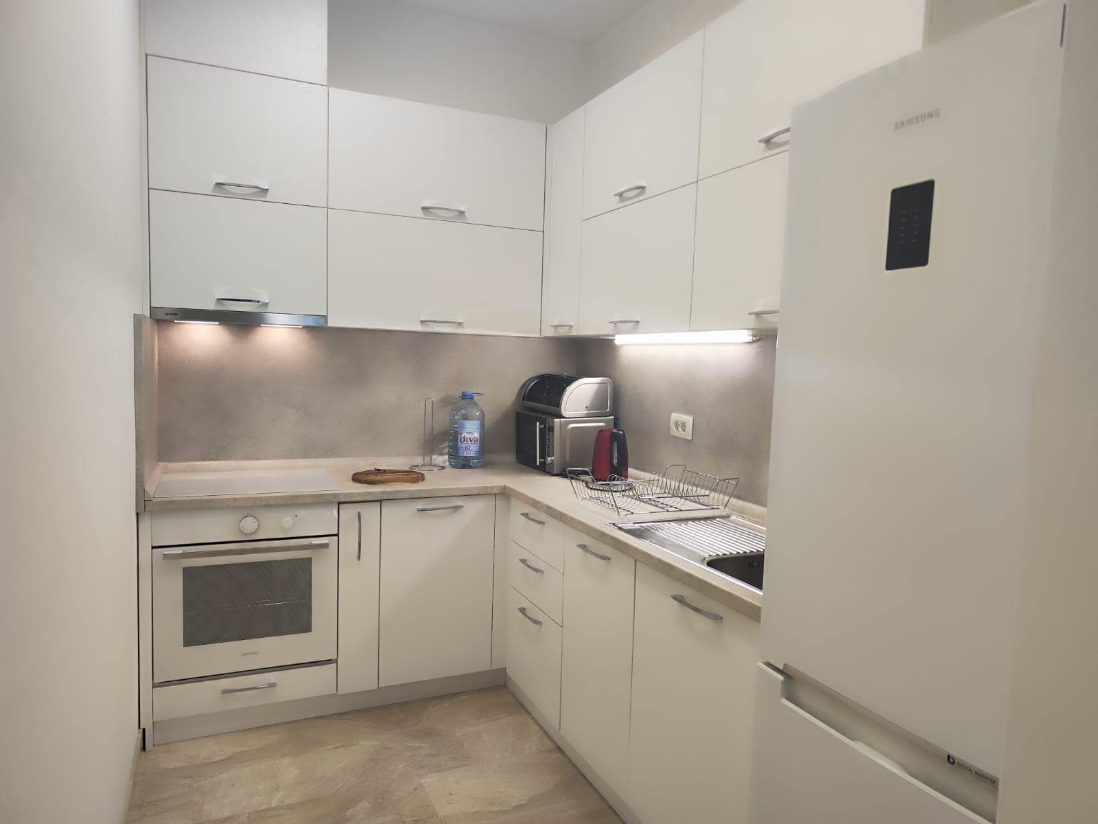 Modern white kitchen in an apartment in Budva, Montenegro: built-in appliances, cabinets, and under-cabinet lighting.