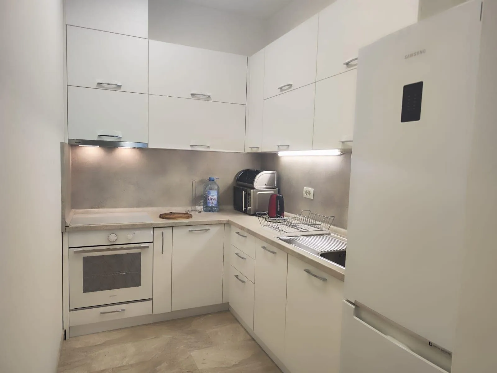 Modern kitchen featuring white cabinets, built-in oven, Samsung fridge, sink, and countertop appliances.