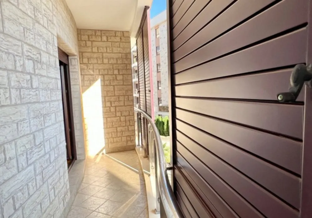 Balcony with stone wall, tiled floor, and metal railing. A brown roller shutter is visible on the right side.