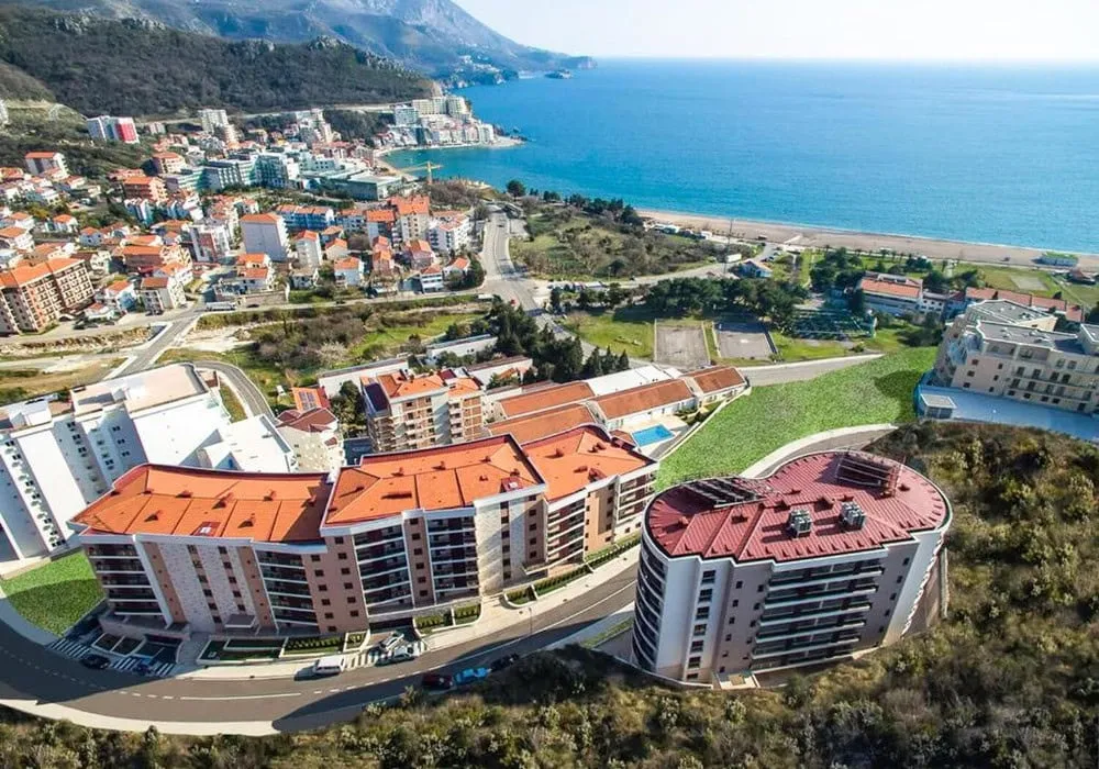 Aerial view of a coastal town featuring multi-story buildings, sea, and mountains in the background.