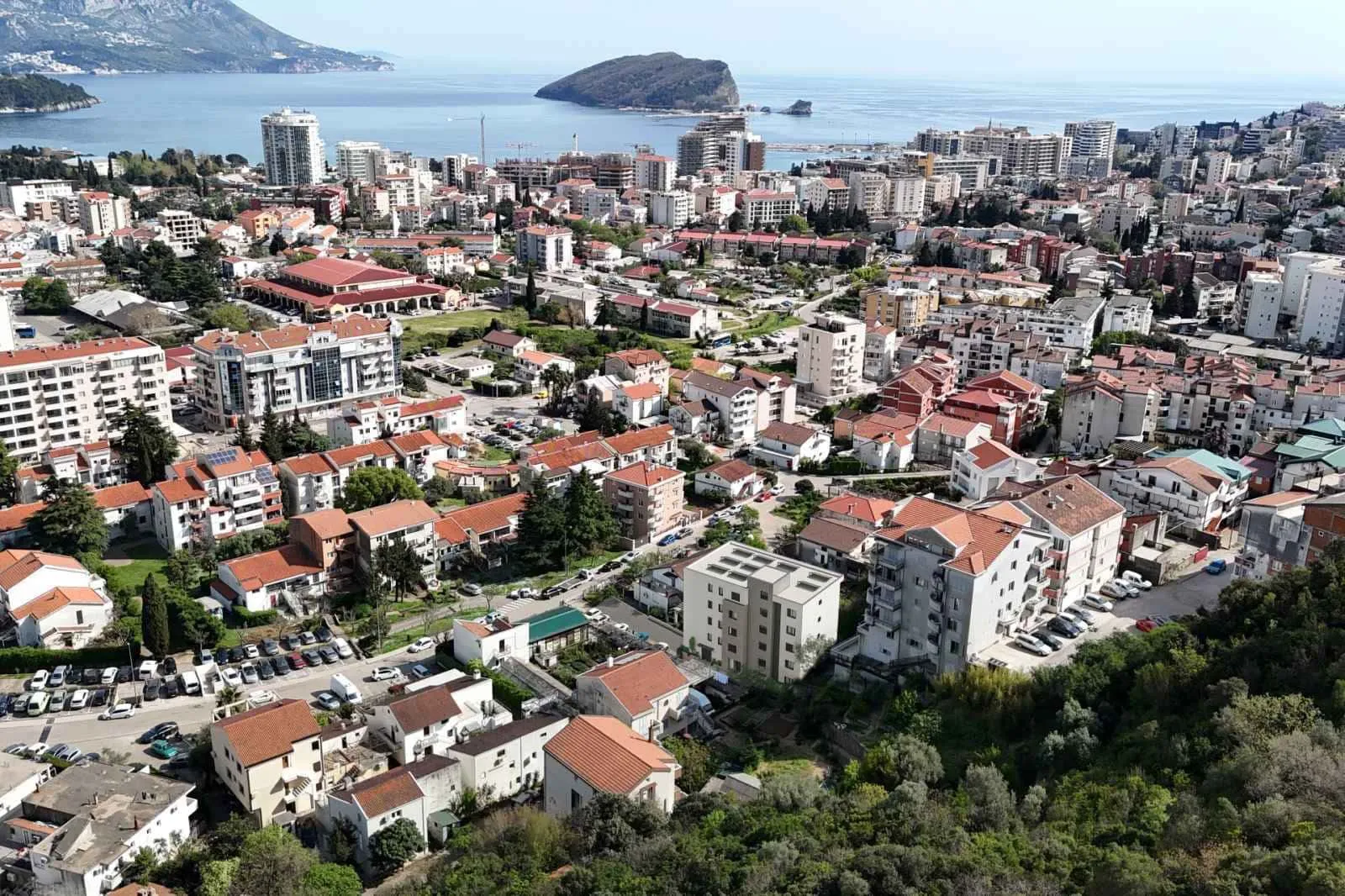 Aerial view of a coastal city featuring dense residential buildings, parking areas, and the sea in the background.