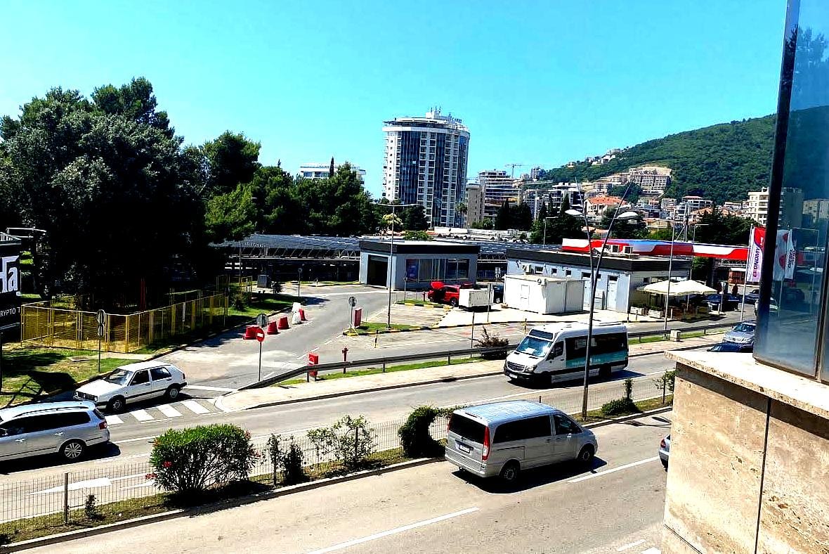 View from the apartment window in central Budva, Montenegro: city buildings, road, cars, and mountains in the background.