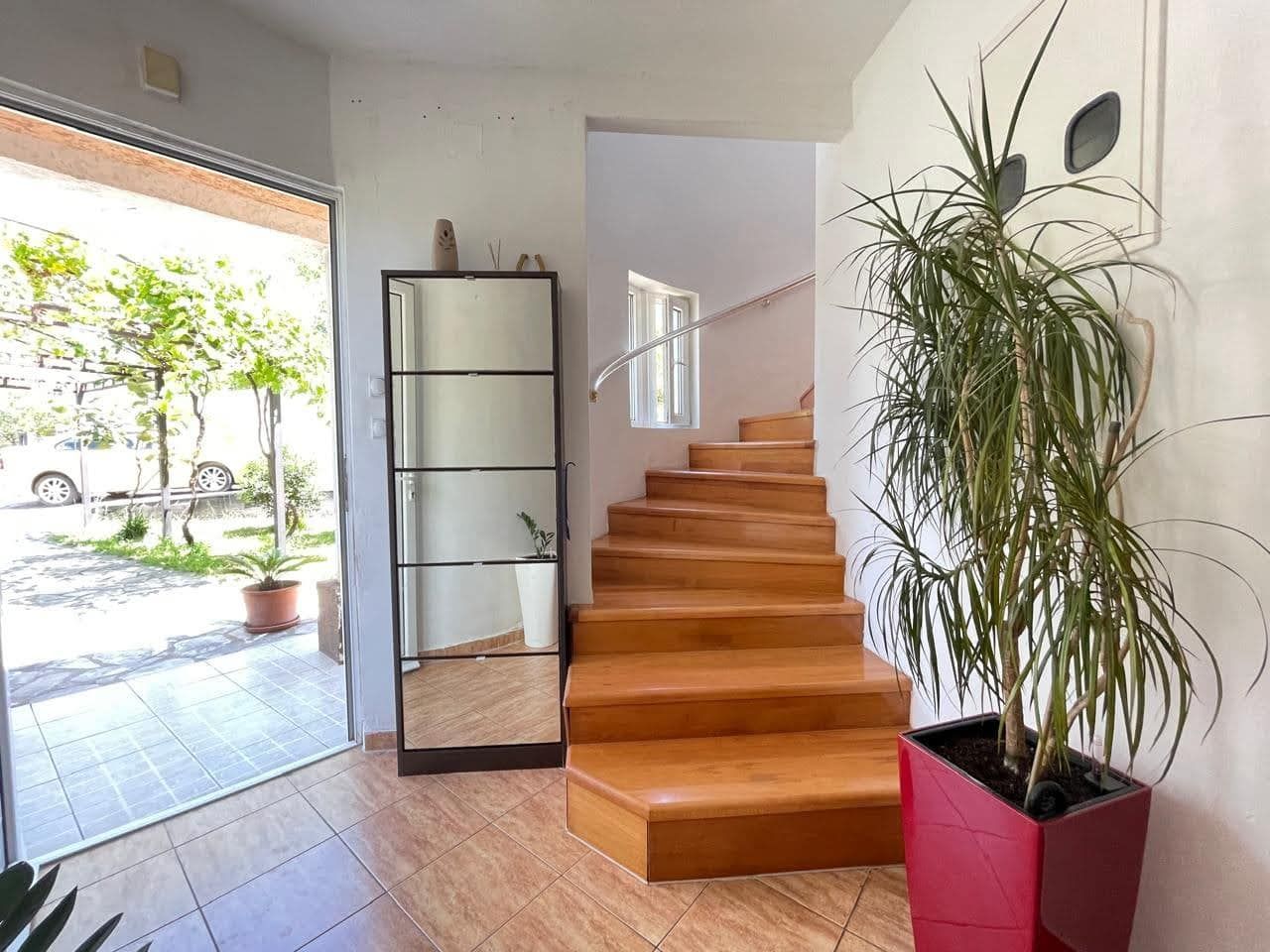Entrance hall with a wooden staircase and mirror in a house, city of Bar, Montenegro. View of the terrace and garden through the glass door.