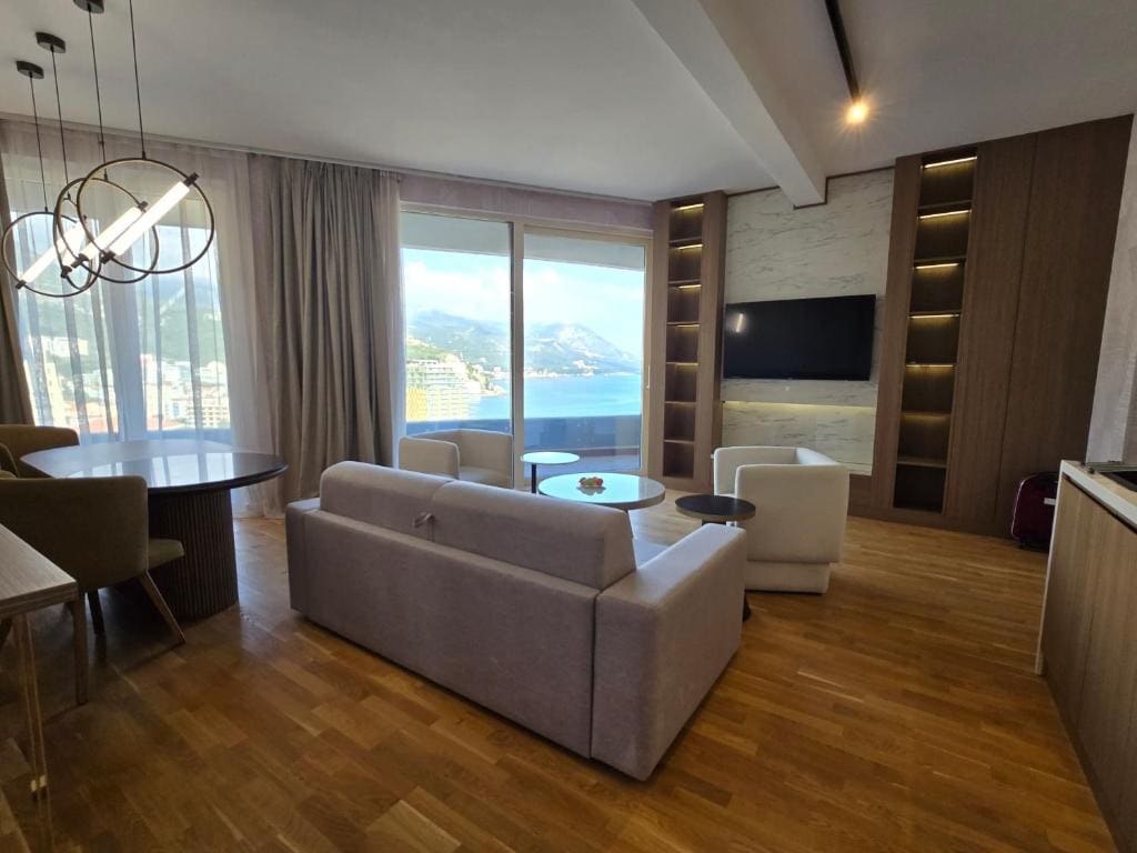 Modern living room with sea view in an apartment, Becici, Montenegro: light furniture, parquet flooring, and panoramic windows.