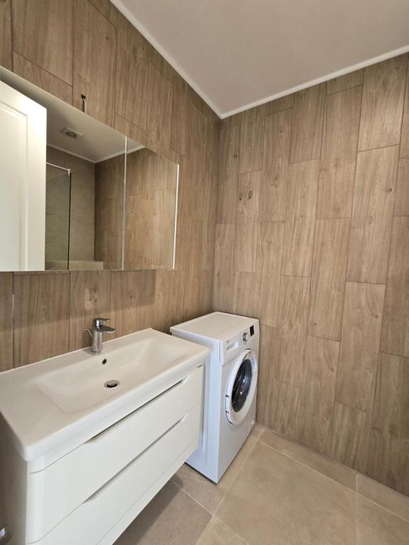 Modern bathroom in an apartment in Bečići, Montenegro: white vanity with sink, washing machine, and wood-look tiles.