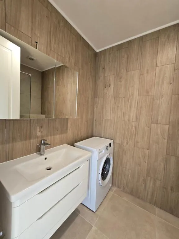Bathroom featuring a white vanity sink, large mirror, and washing machine against wood-effect walls.