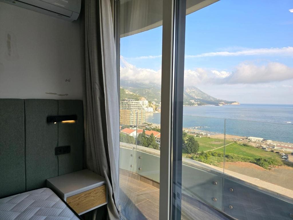 Bedroom with panoramic sea and mountain views in an apartment, Becici, Montenegro. Modern finishes and a glass balcony.