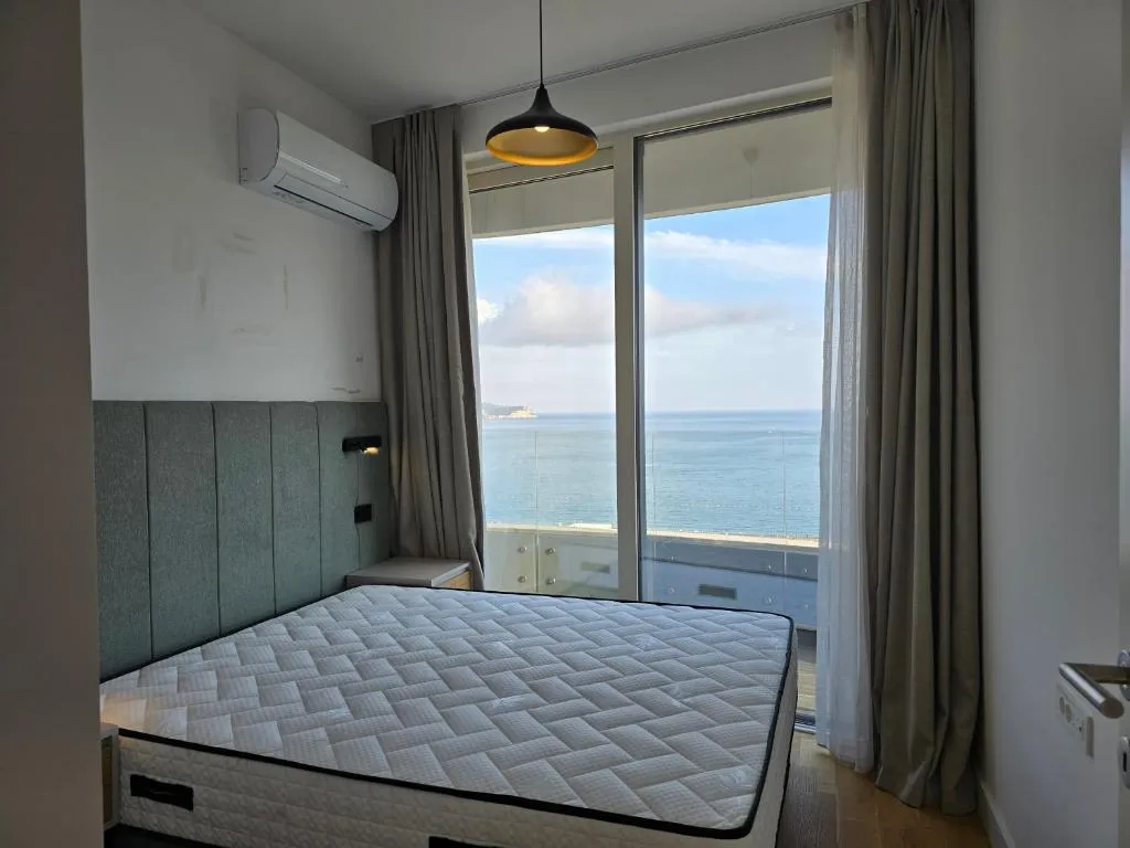 Bedroom featuring a mattress, upholstered headboard, and AC unit. Large window offers a panoramic sea view.