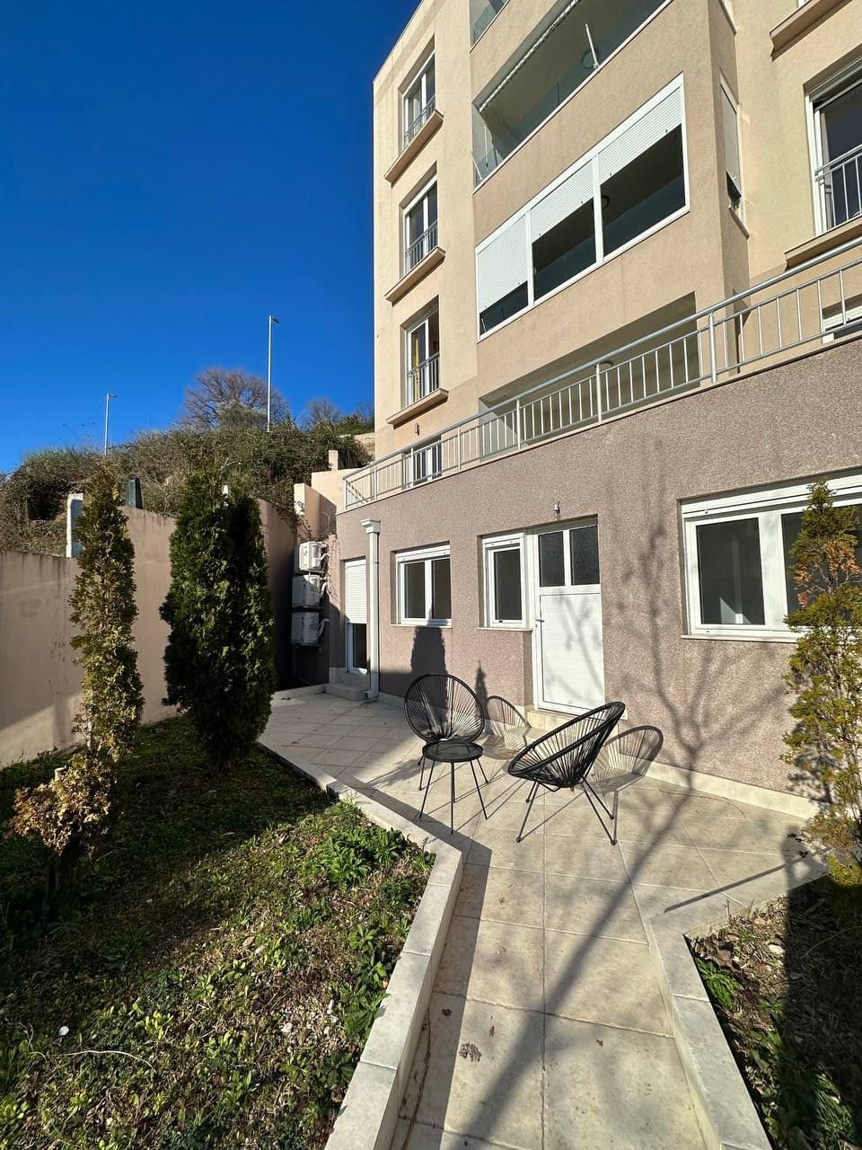 Terrace with garden furniture by a modern residential building in Tivat, Montenegro: view of the courtyard area and facade.