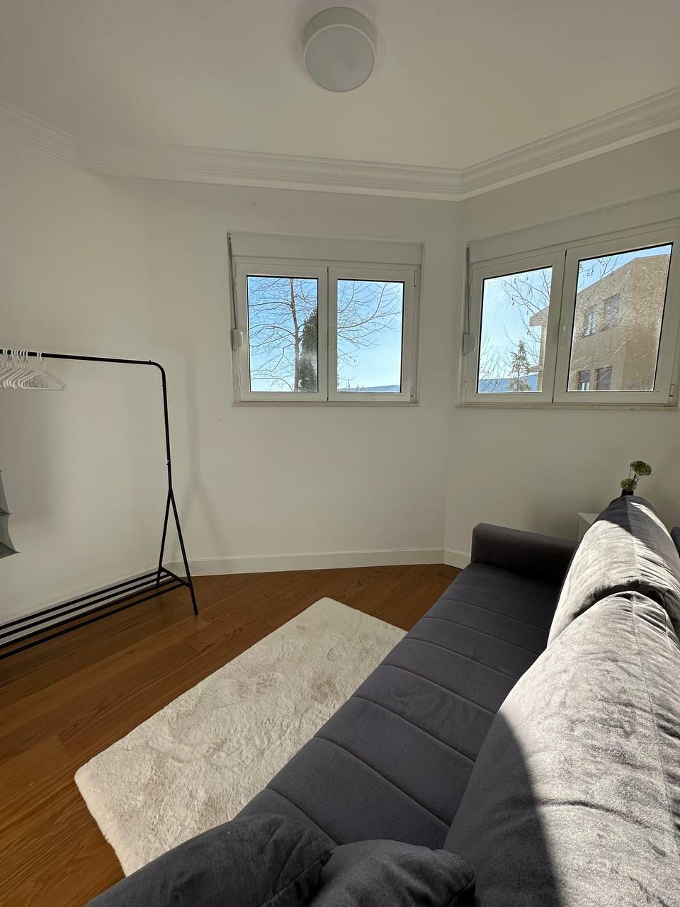 Bright living room with a gray sofa and parquet flooring in an apartment for sale in Tivat, Montenegro. View of nature from the window.