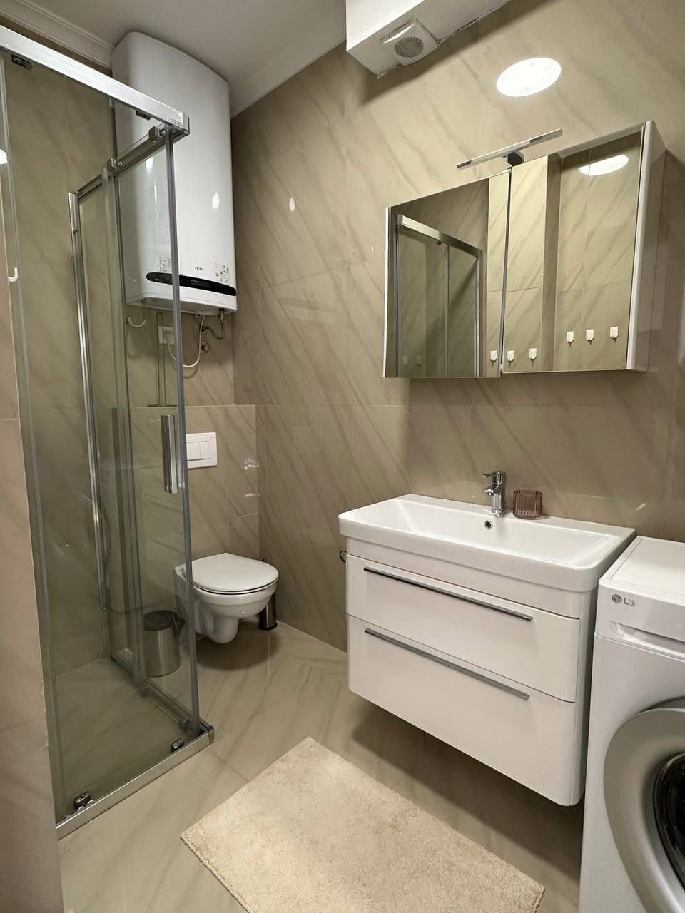 Modern bathroom in an apartment in Tivat, Montenegro: shower cabin, vanity with sink, and washing machine.