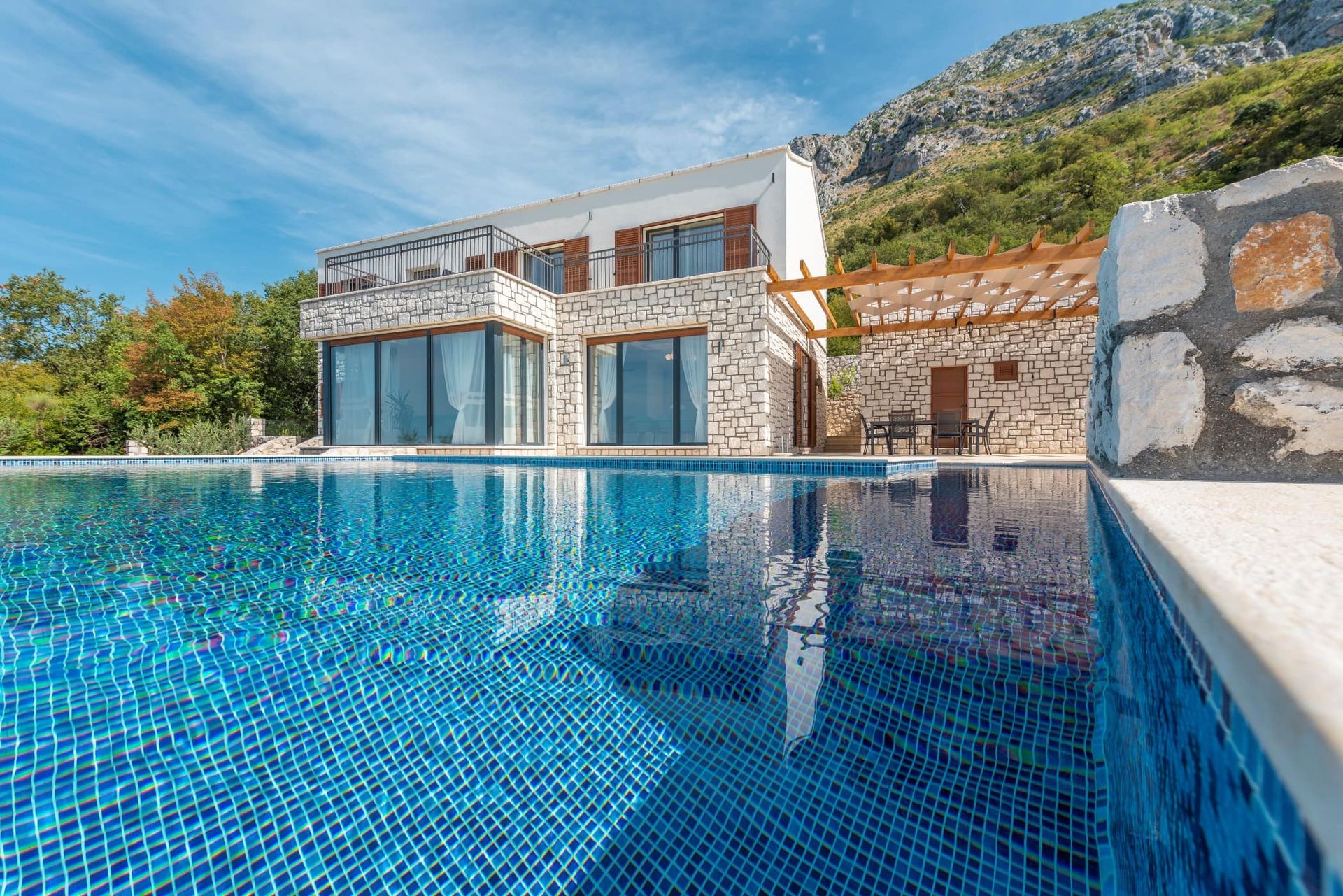 Modern villa with a pool and stone cladding in Reževići, Montenegro: view of the house with a terrace and mountains.