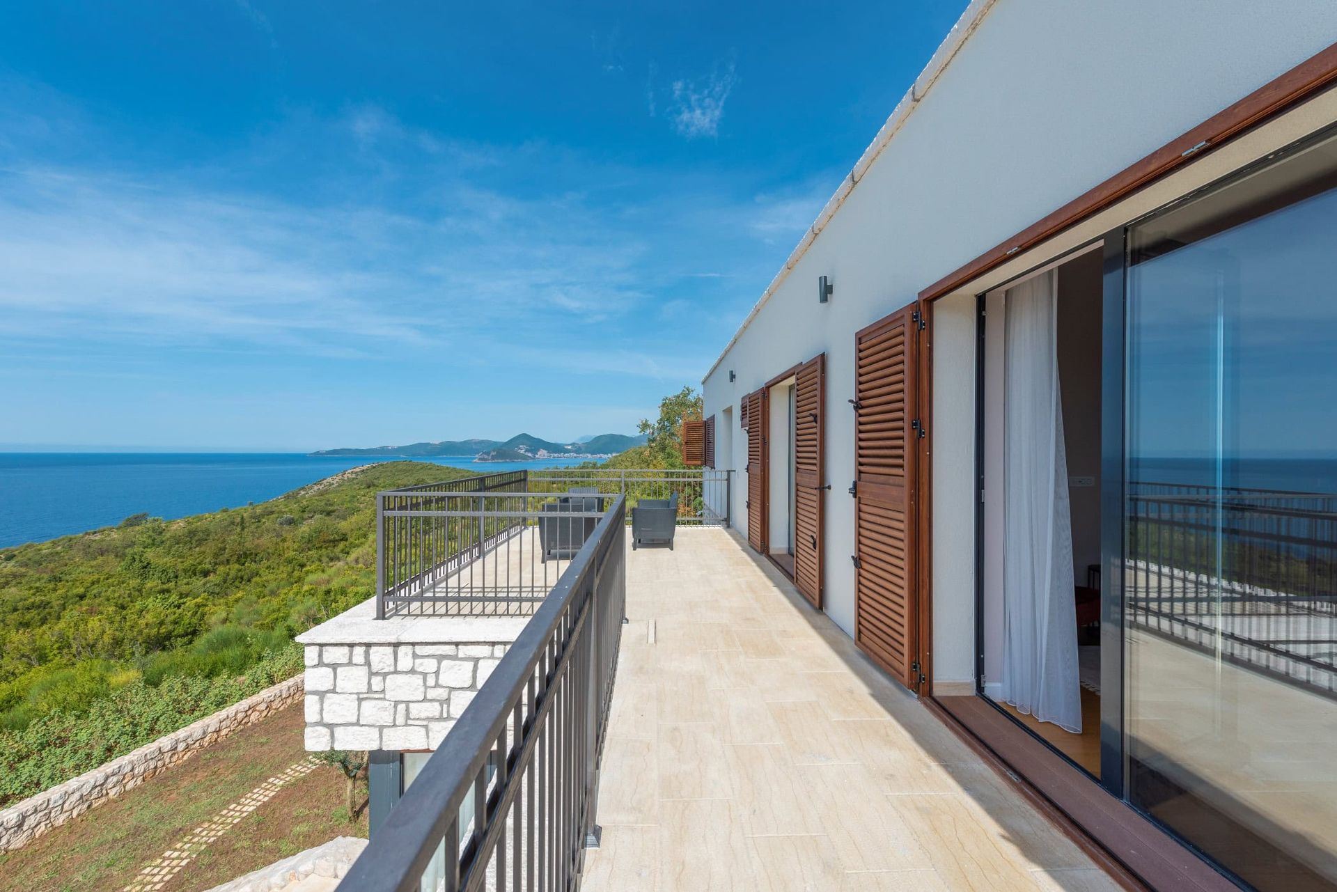 Spacious terrace of a house in Reževići, Montenegro, with panoramic sea views, stone finishes, and wooden shutters.