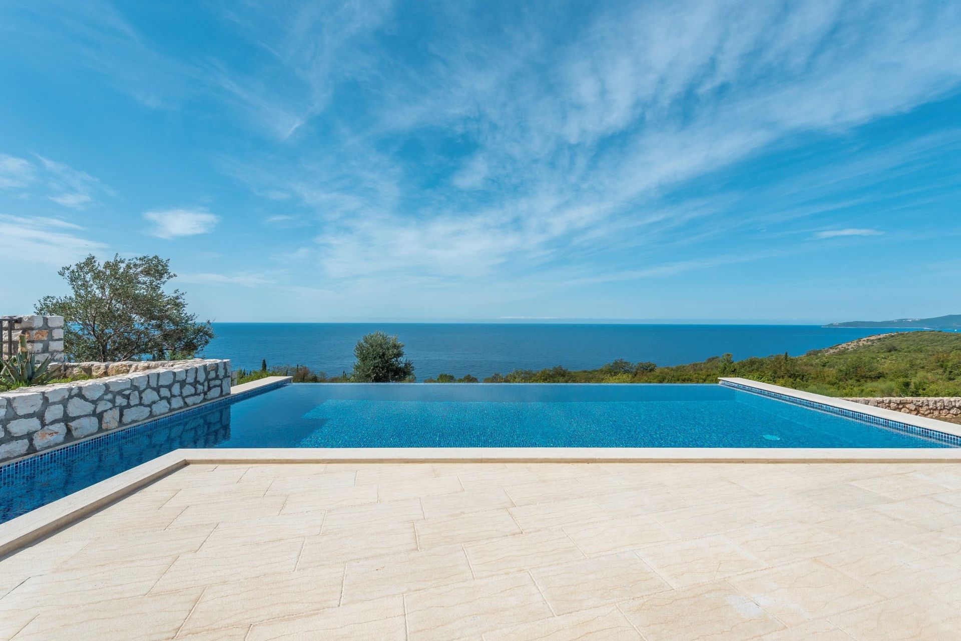 Infinity pool with sea view at a house in Reževići, Montenegro: stone terrace finish and panoramic seascape.