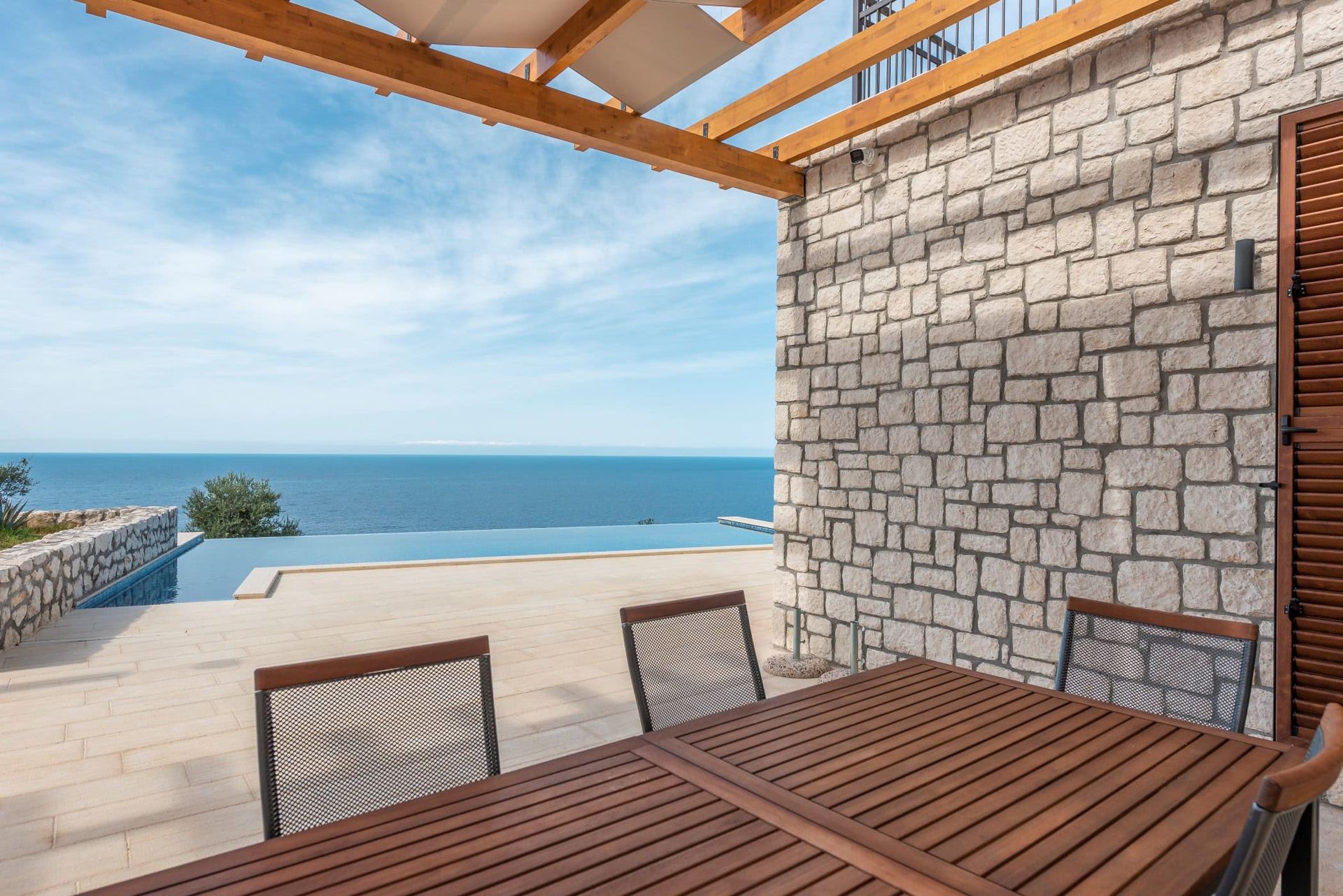 Terrace with an infinity pool and sea view in a house, Reževići, Montenegro: stone finishes and wooden furniture.