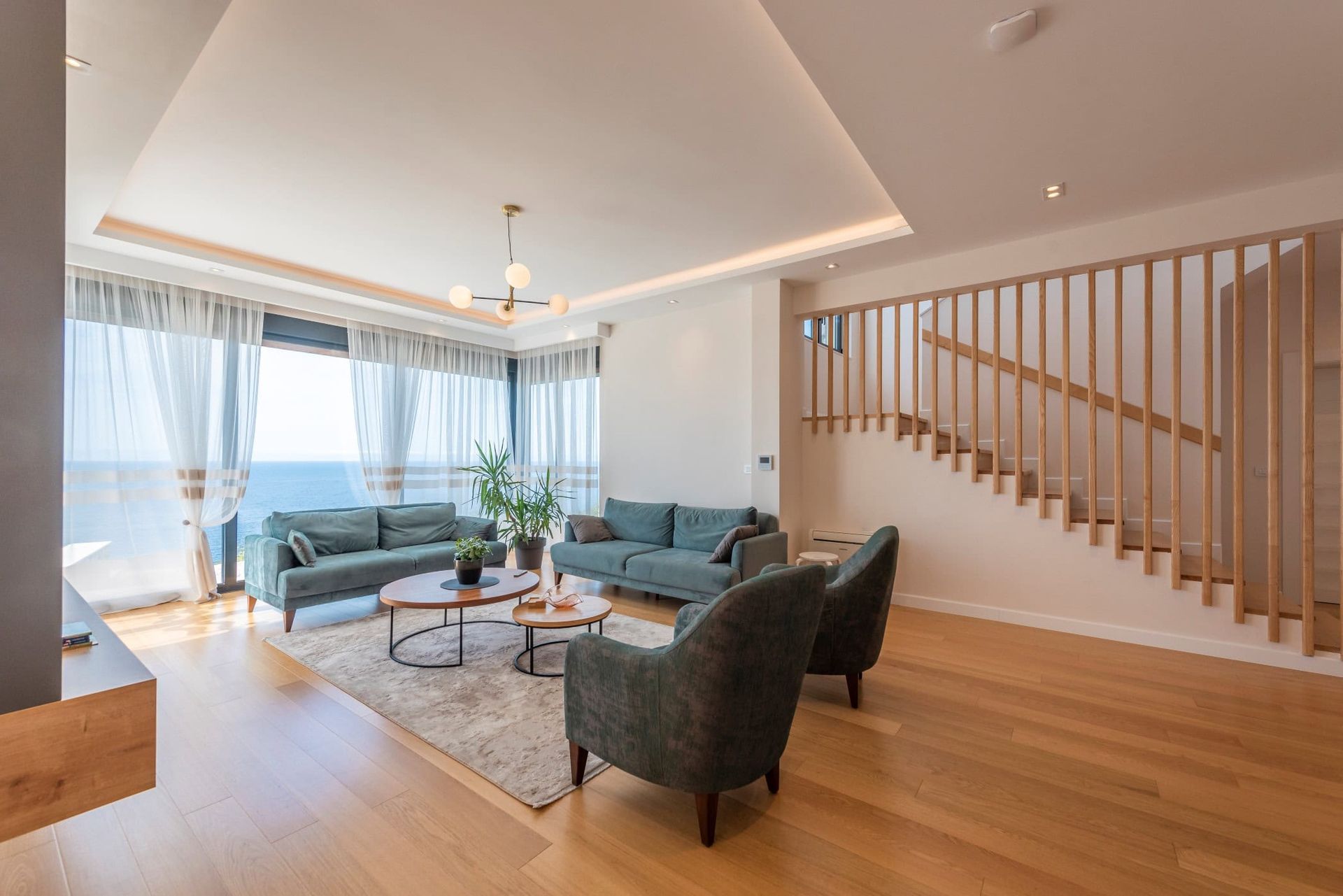 Modern living room in a house in Reževići, Montenegro: panoramic sea view, soft seating, and a wooden staircase.