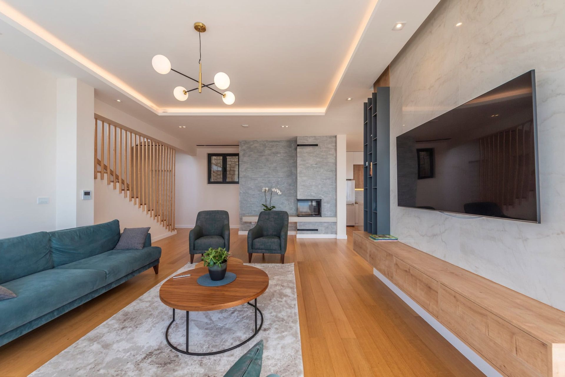 Modern living room with a fireplace and wooden staircase in a house, Reževići, Montenegro. Interior with soft seating.