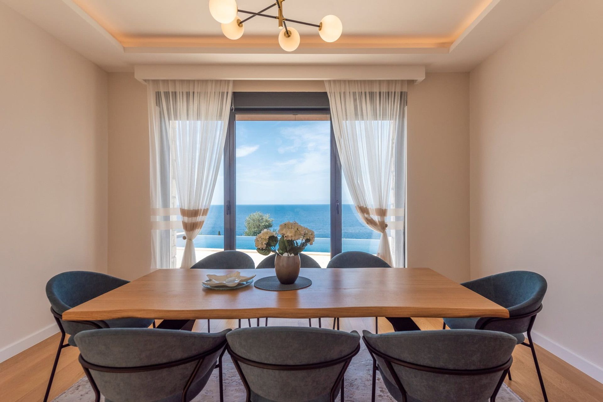 Dining area in a house in Reževići, Montenegro: a wooden table, gray chairs, and a panoramic sea view from the window.