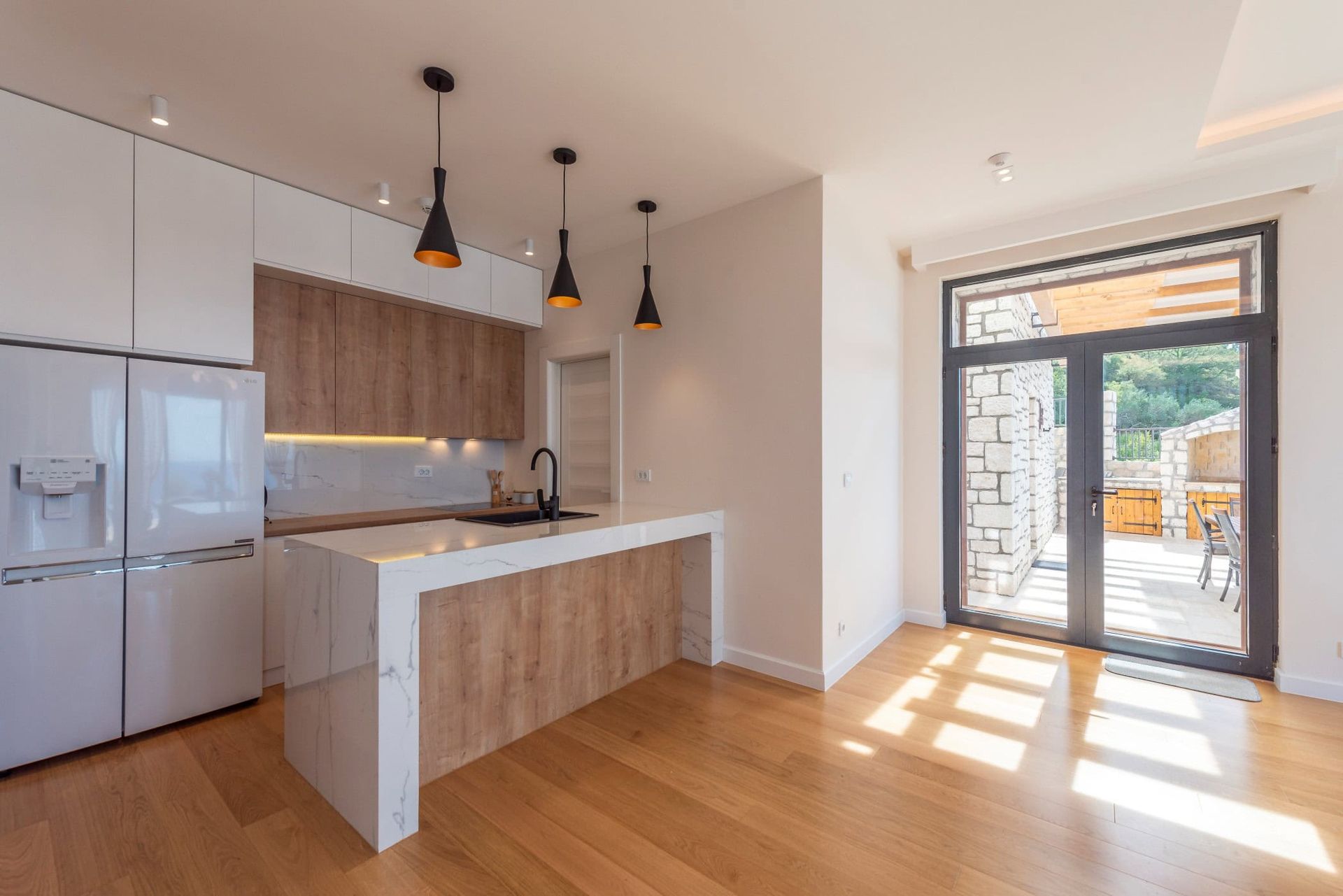 Modern kitchen with an island in a house in Reževići, Montenegro: light-colored cabinetry, marble countertop, and access to the terrace.