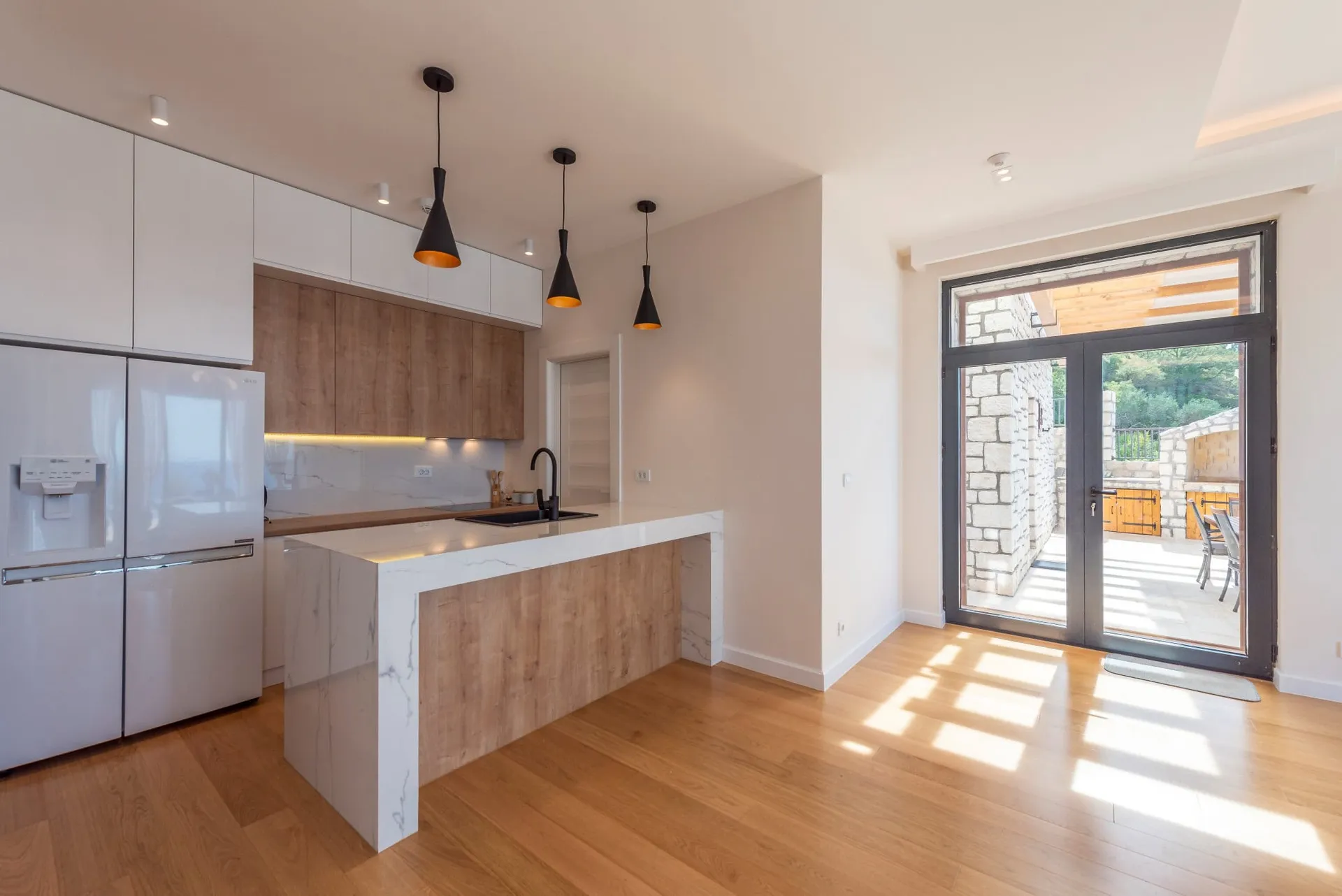 Modern kitchen featuring a white marble island, wood cabinetry, refrigerator, and black pendant lights.