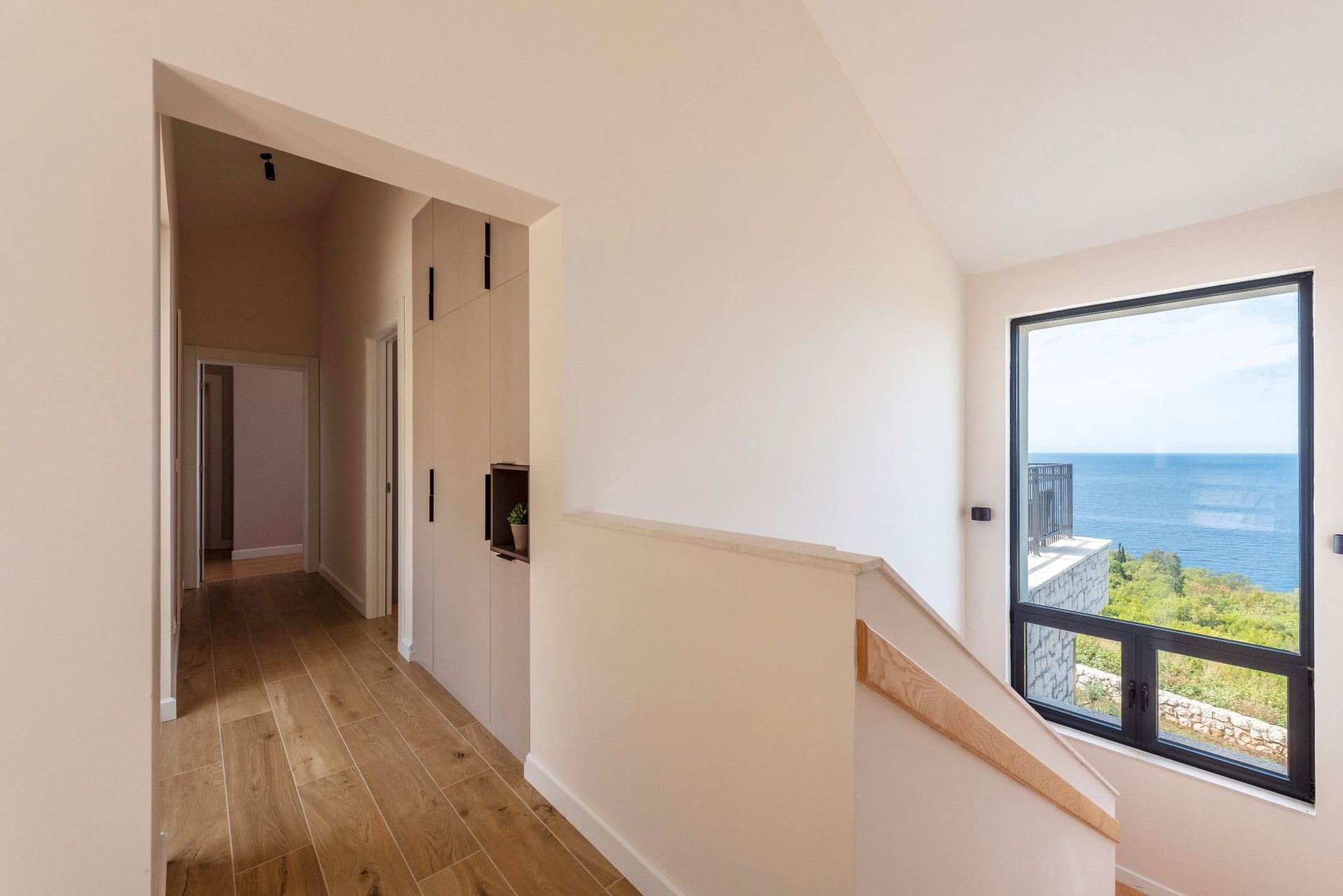 Interior of a house in Reževići, Montenegro: a bright hallway with a panoramic window and sea view, built-in wardrobe, and staircase.