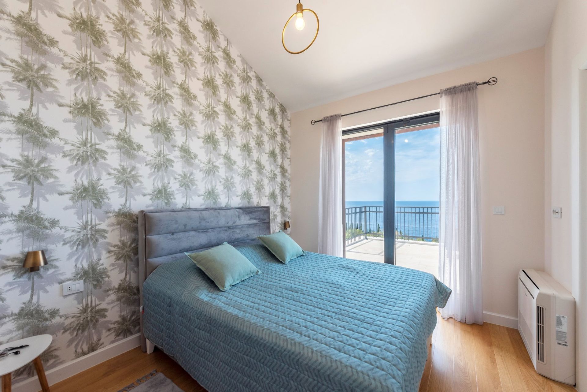 Bedroom in a house in Reževići, Montenegro: a double bed, palm-pattern wallpaper, and a panoramic sea view from the terrace.
