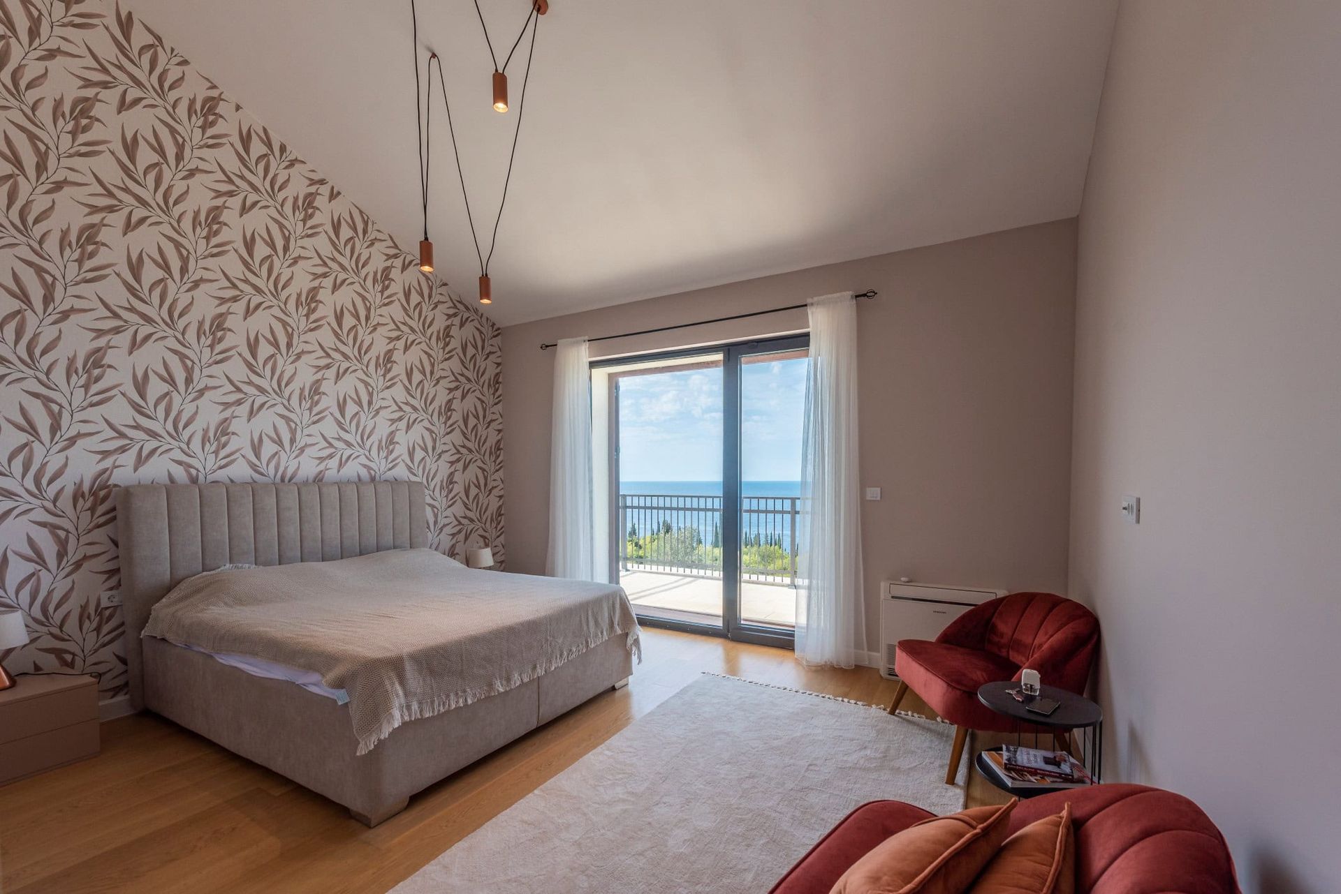 Bedroom in a house in Reževići, Montenegro: double bed, accent wall, red armchairs, and sea view from the terrace.