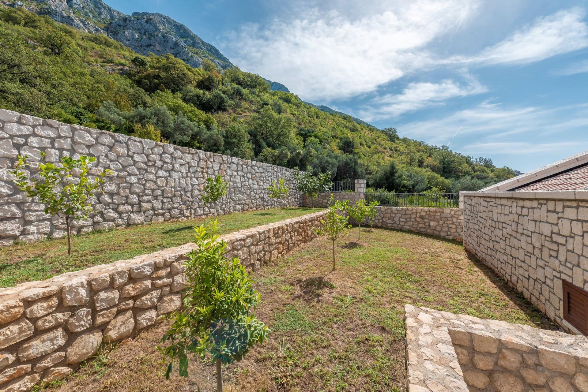 Well-kept garden with stone terraces and young trees by the house in Reževići, Montenegro, mountain view.