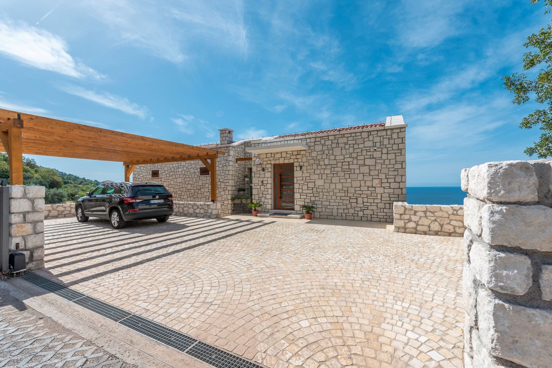 Stone house in Rezevici, Montenegro: natural stone facade, parking with a wooden canopy, and sea view.
