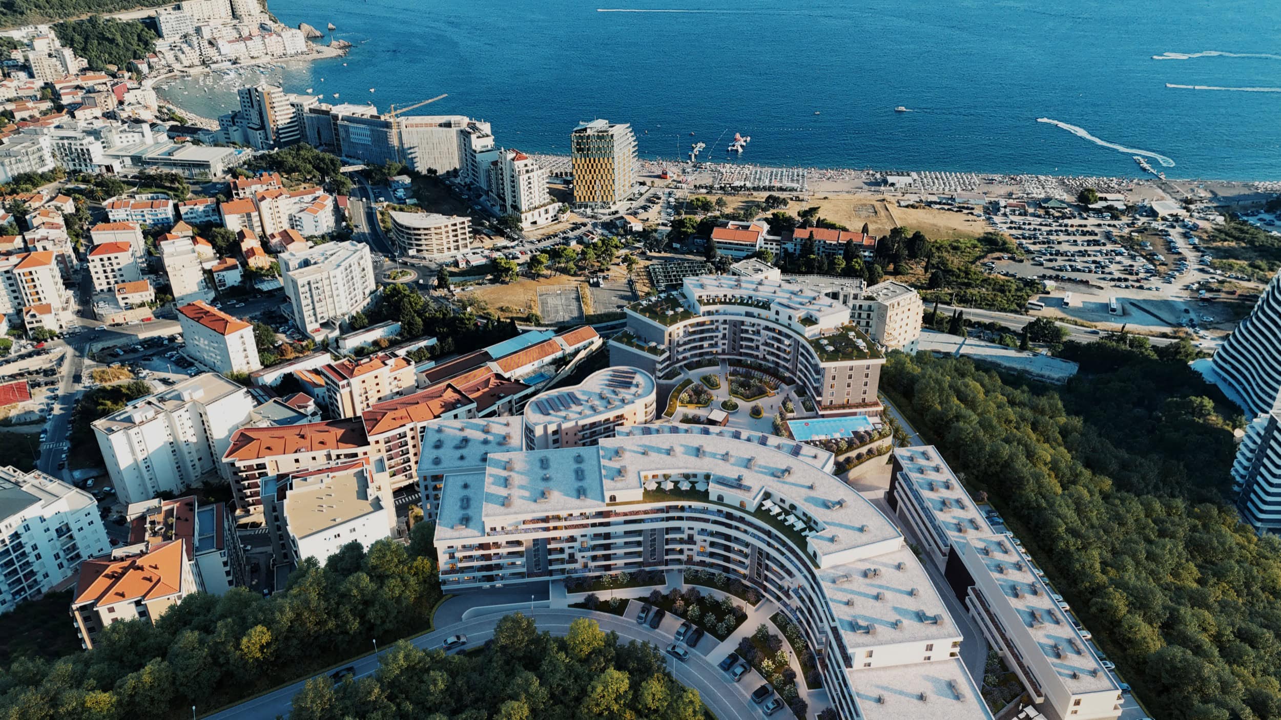 Aerial view of a modern residential complex in Bečići, Montenegro, with a swimming pool and panoramic view of the Adriatic Sea.