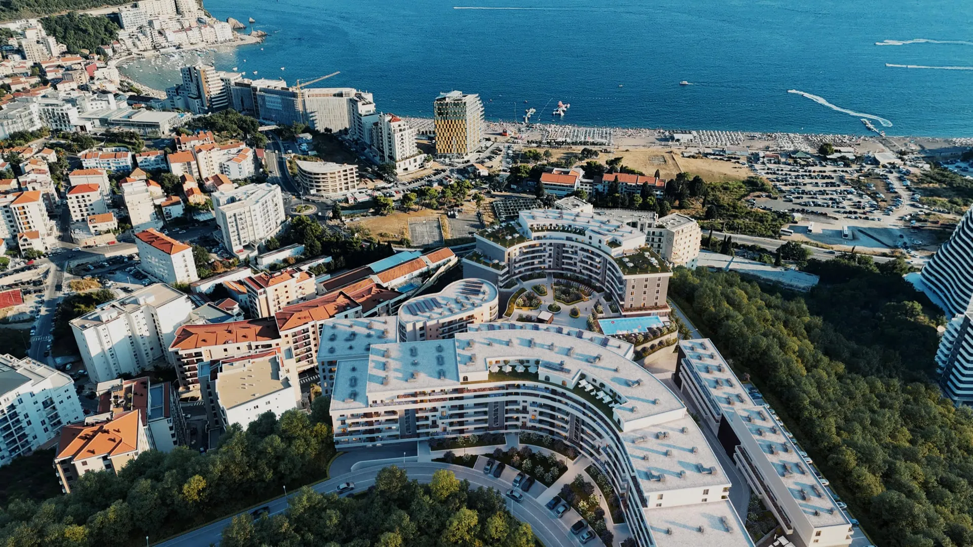 Aerial view of a large coastal resort complex with curved buildings, a beach, and parking areas.