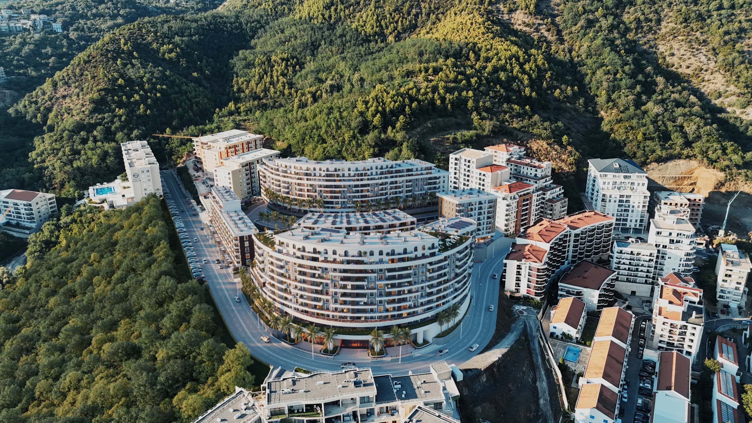 Aerial view of a modern residential complex in Bečići, Montenegro, surrounded by green mountains and infrastructure.