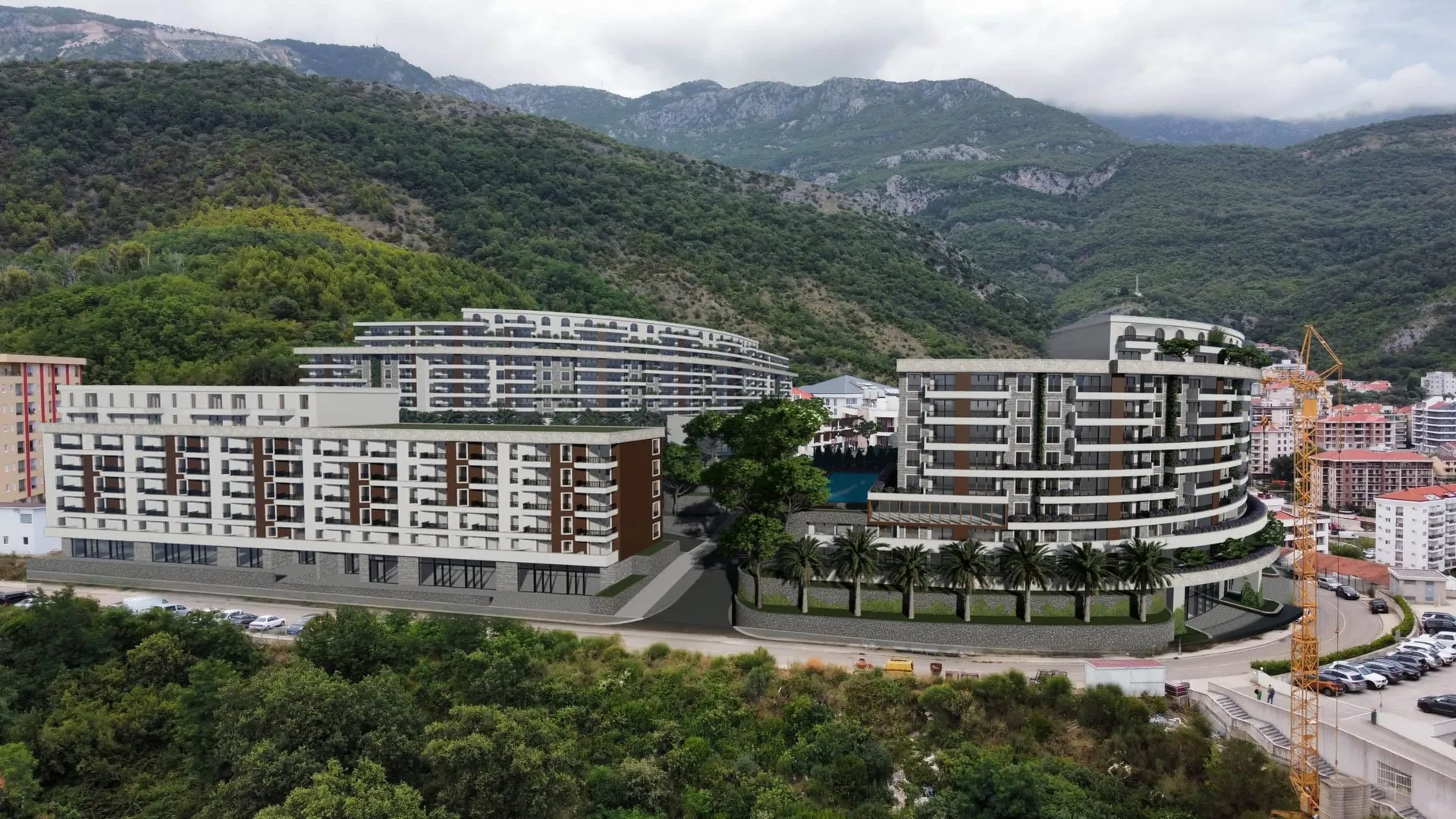 Aerial view of a residential complex with multiple multi-story buildings set against green mountains and a construction crane.