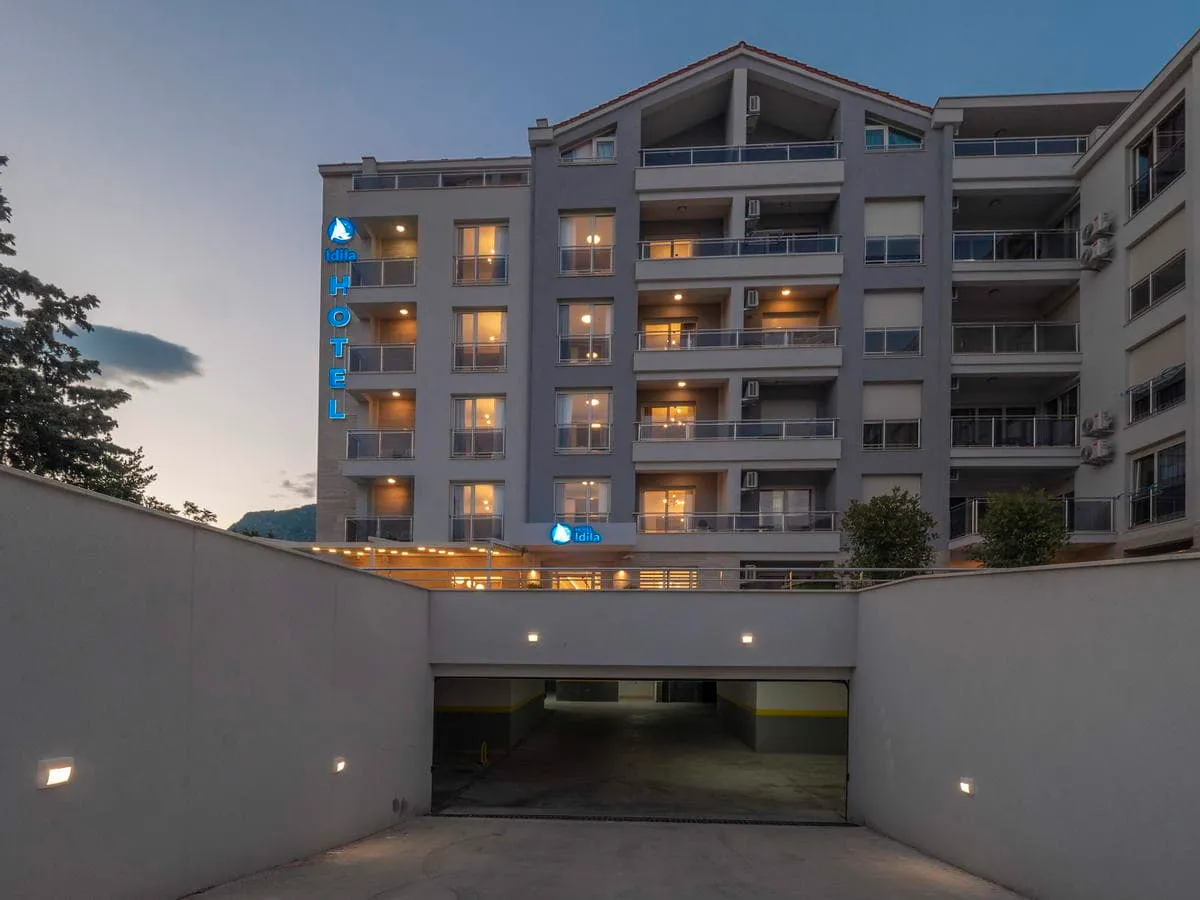 Exterior view of the multi-story Idilia hotel featuring balconies and an underground parking entrance at dusk.