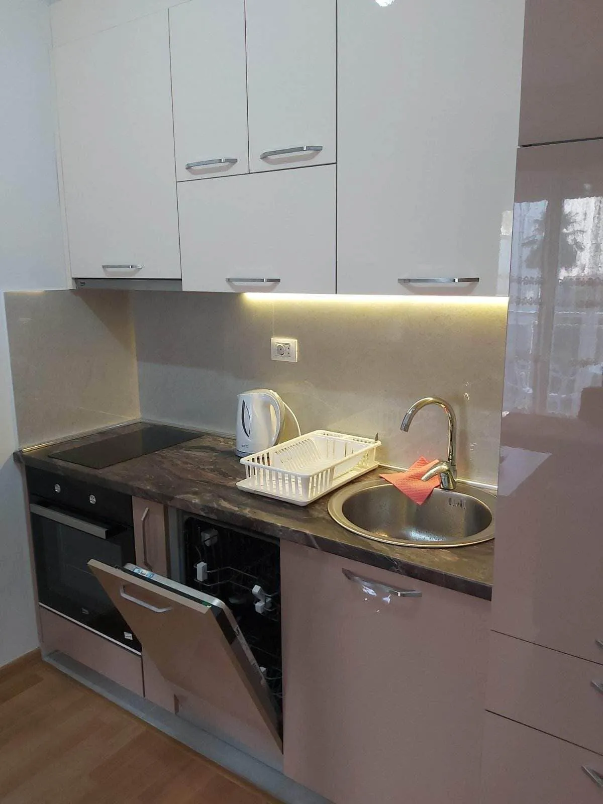 Kitchen with white upper cabinets, pink lower units, sink, cooktop, and an open dishwasher under the dark countertop.