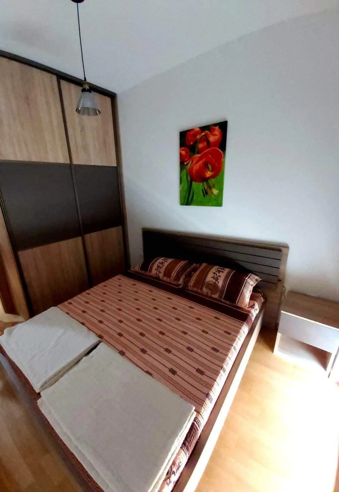 Bedroom featuring a double bed with striped bedding, a wood and dark panel wardrobe, and floral wall art.
