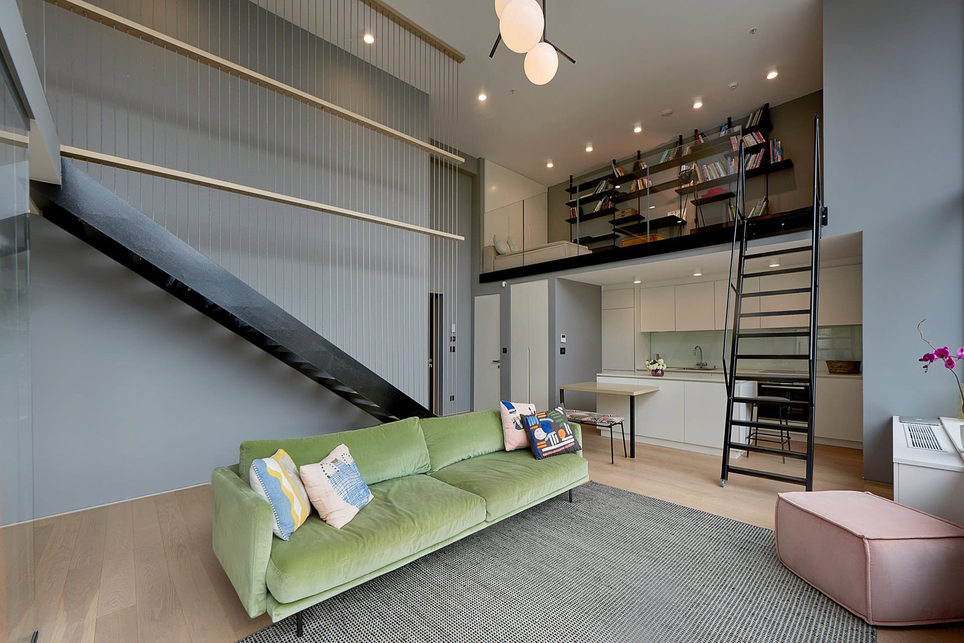Modern duplex apartment in Budva, Montenegro: living room with a green sofa, kitchen, and staircase to the mezzanine.