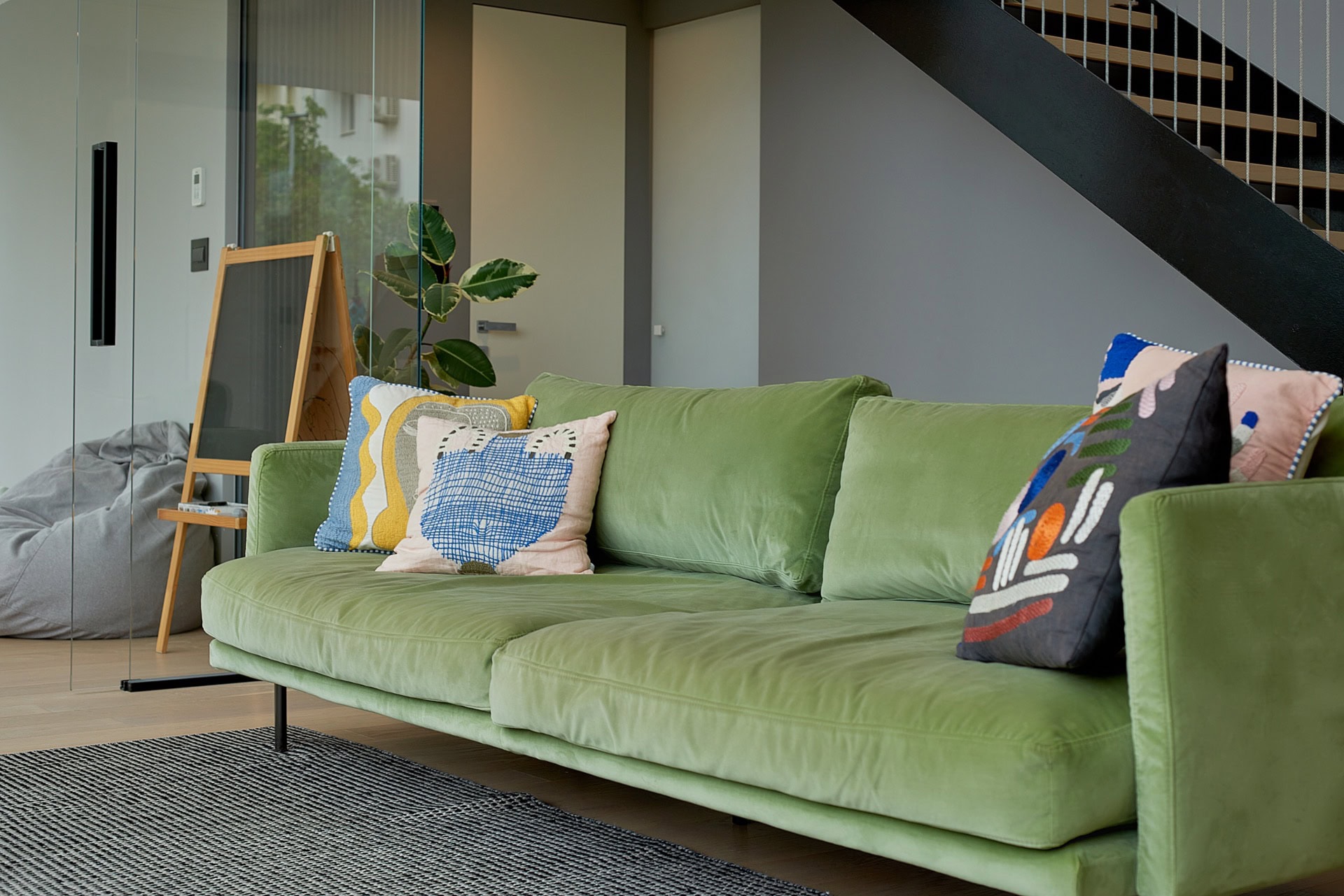 Green velvet sofa in a modern apartment living room in the center of Budva, Montenegro, with a staircase and glass partition.