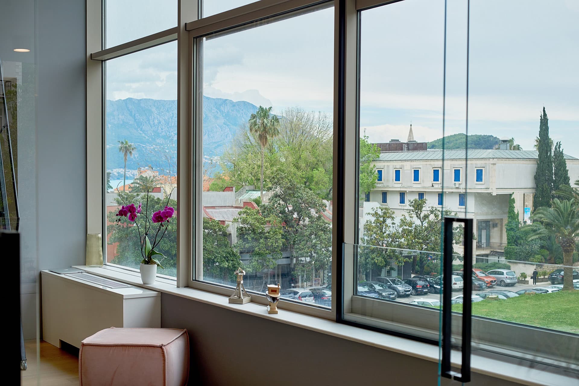 View from the living room’s panoramic windows of the mountains and the city of Budva, Montenegro. Modern interior with a pink pouf.