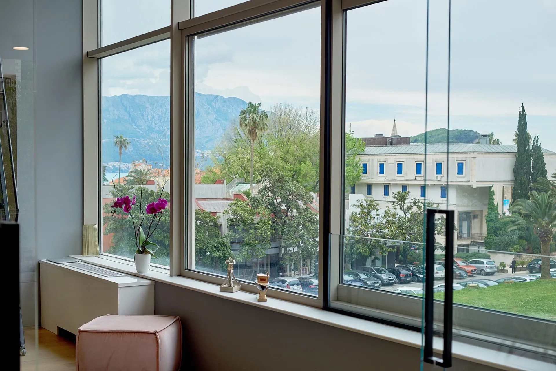 Interior with large windows overlooking mountains and city. Orchid, pink pouf, and decor on the sill.