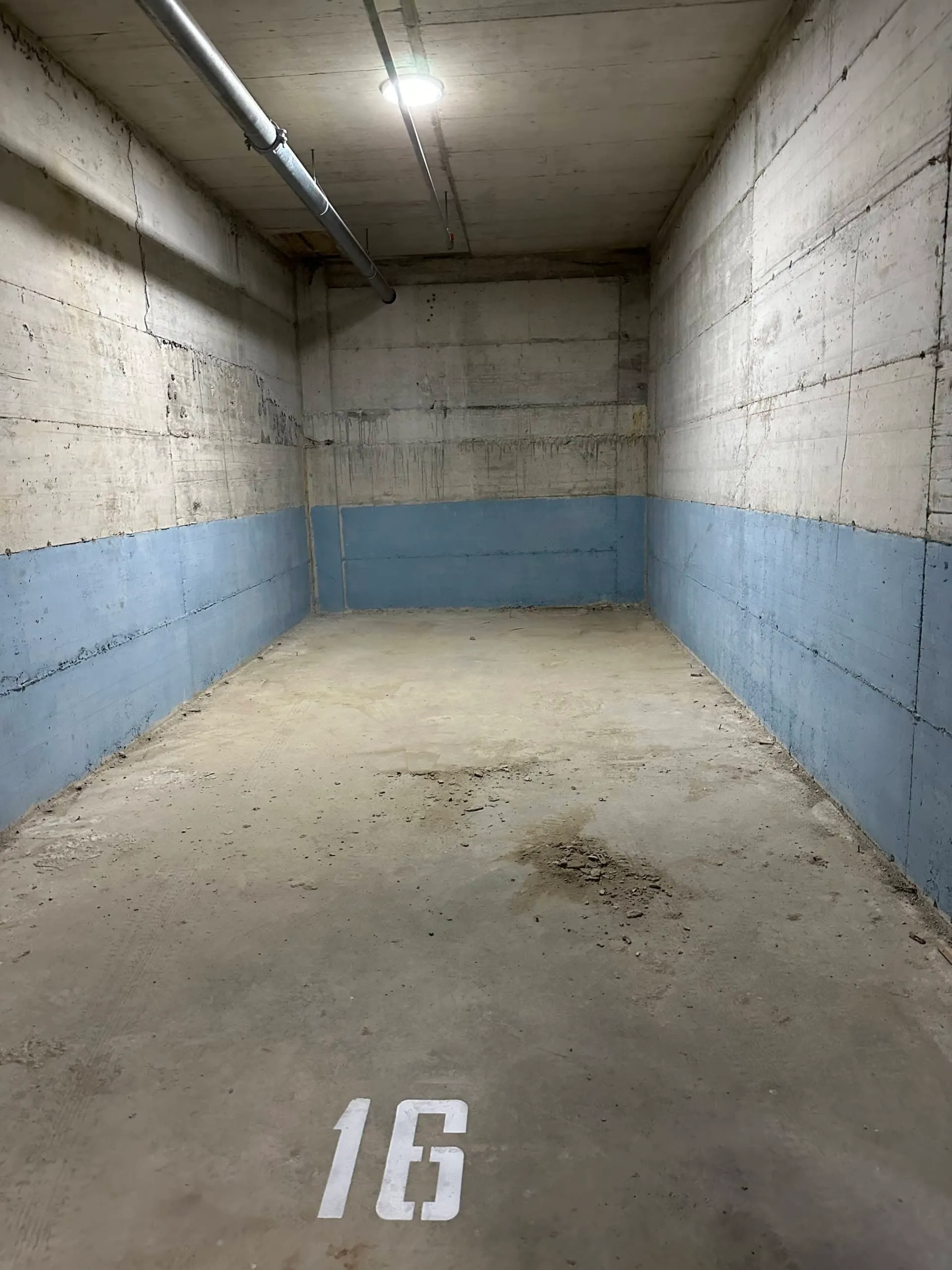 Empty concrete space with number 16 on the floor, likely a parking spot or garage unit.