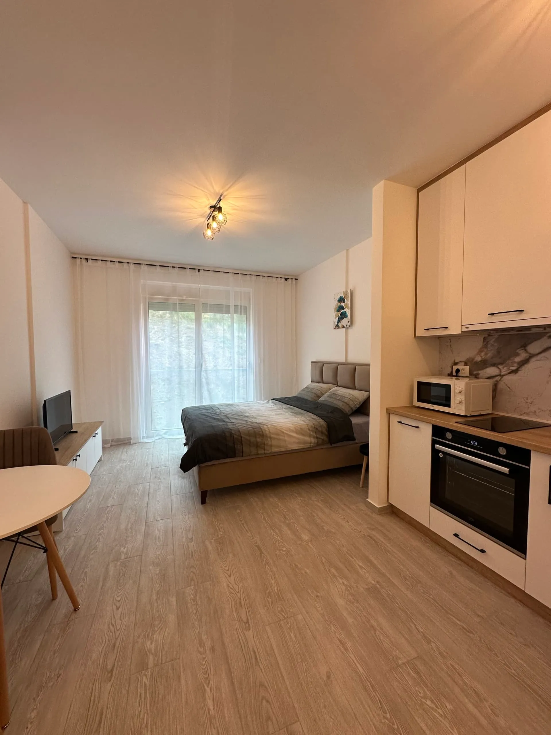 Studio room containing a bed, kitchenette, and TV in an open layout.