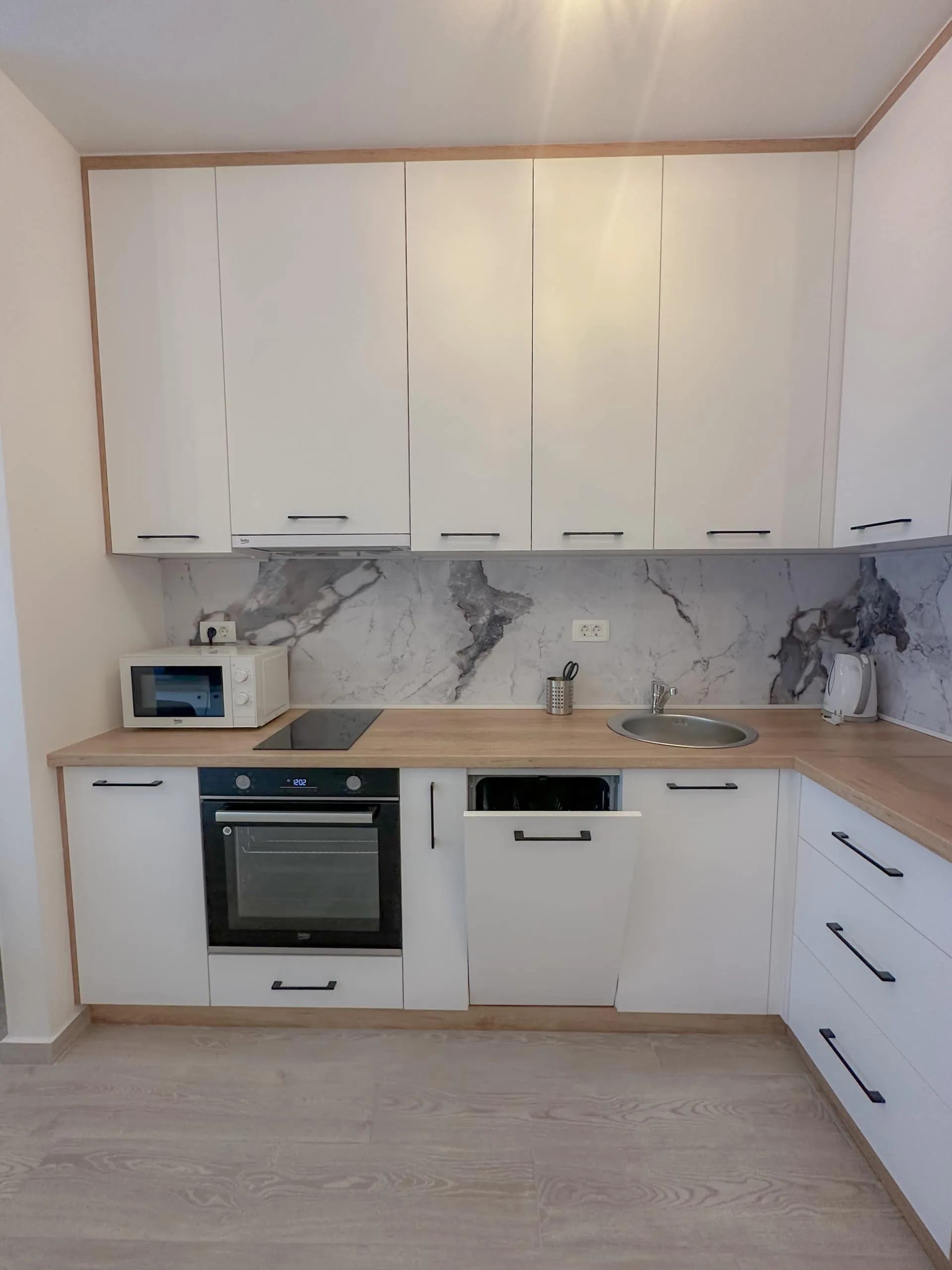 Modern kitchen with white cabinets, wooden countertop, built-in oven and dishwasher, marble backsplash.