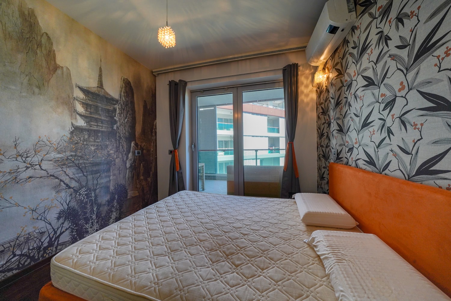 Bedroom in an apartment in Budva, Montenegro: a double bed, designer wallpaper with a landscape, and access to the balcony.
