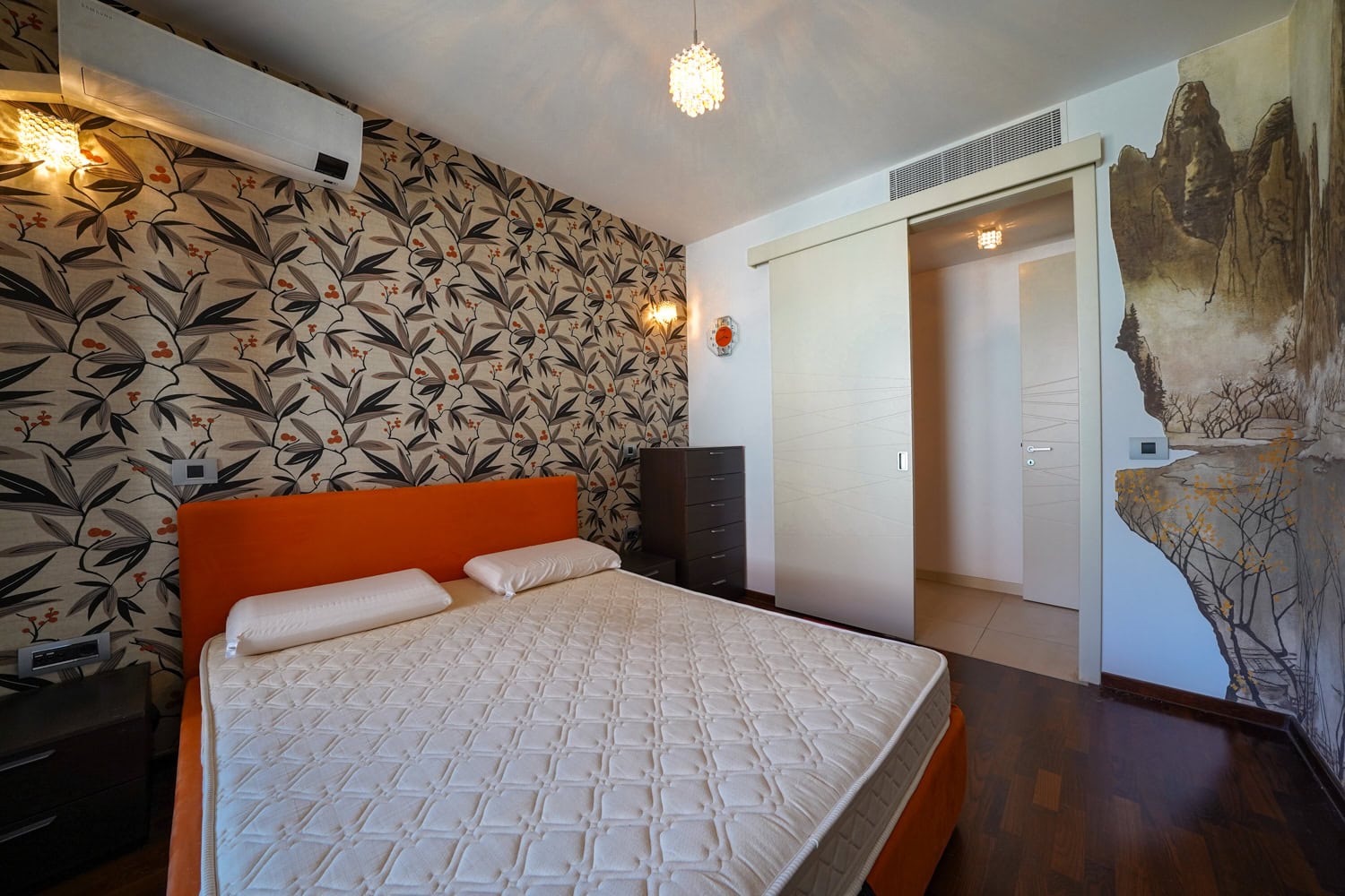 Bedroom in an apartment in Budva, Montenegro: orange bed, floral wallpaper, and sliding doors.