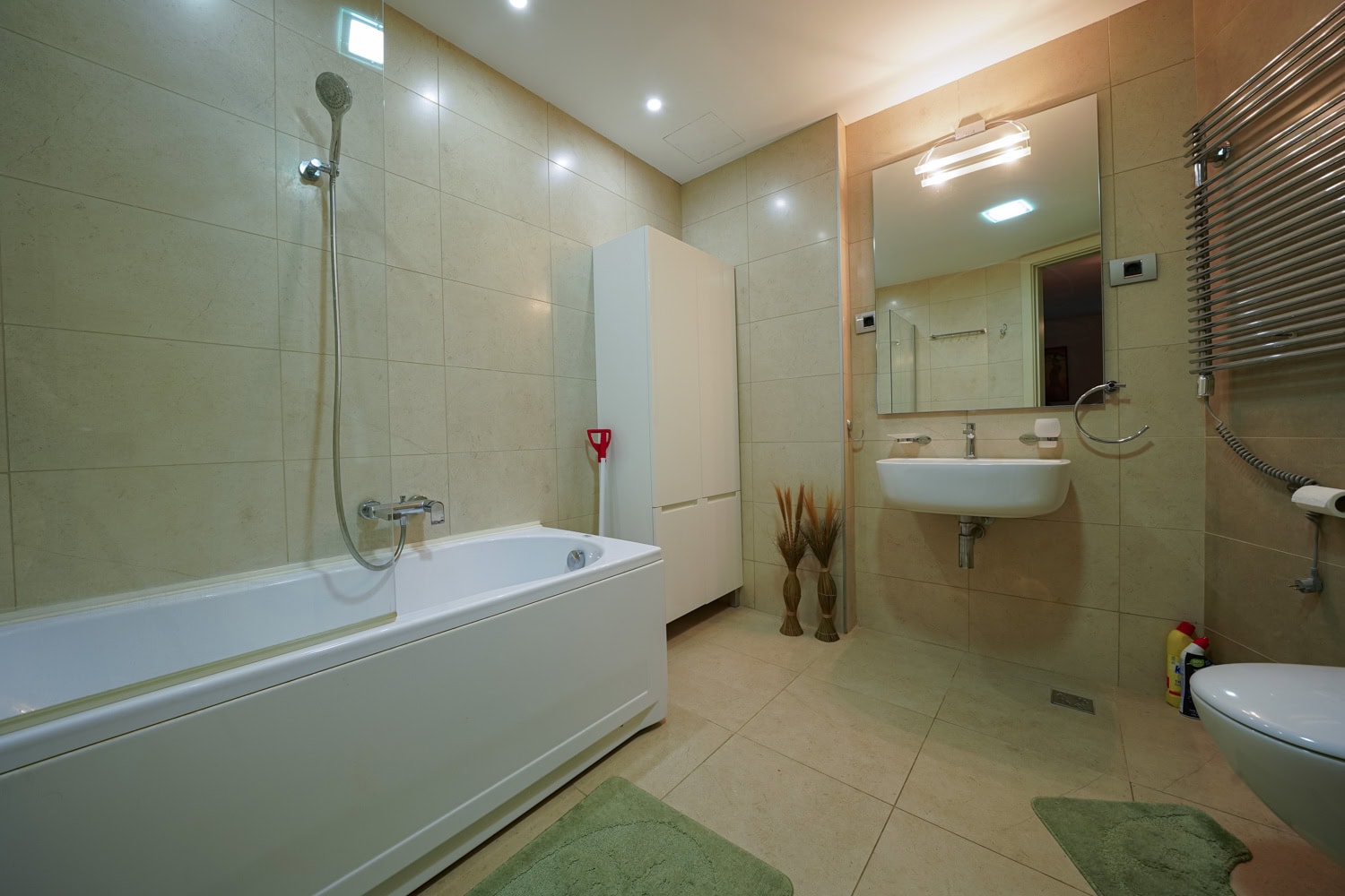 Modern bathroom in an apartment in Budva, Montenegro: white fixtures, beige tiles, and a towel warmer.