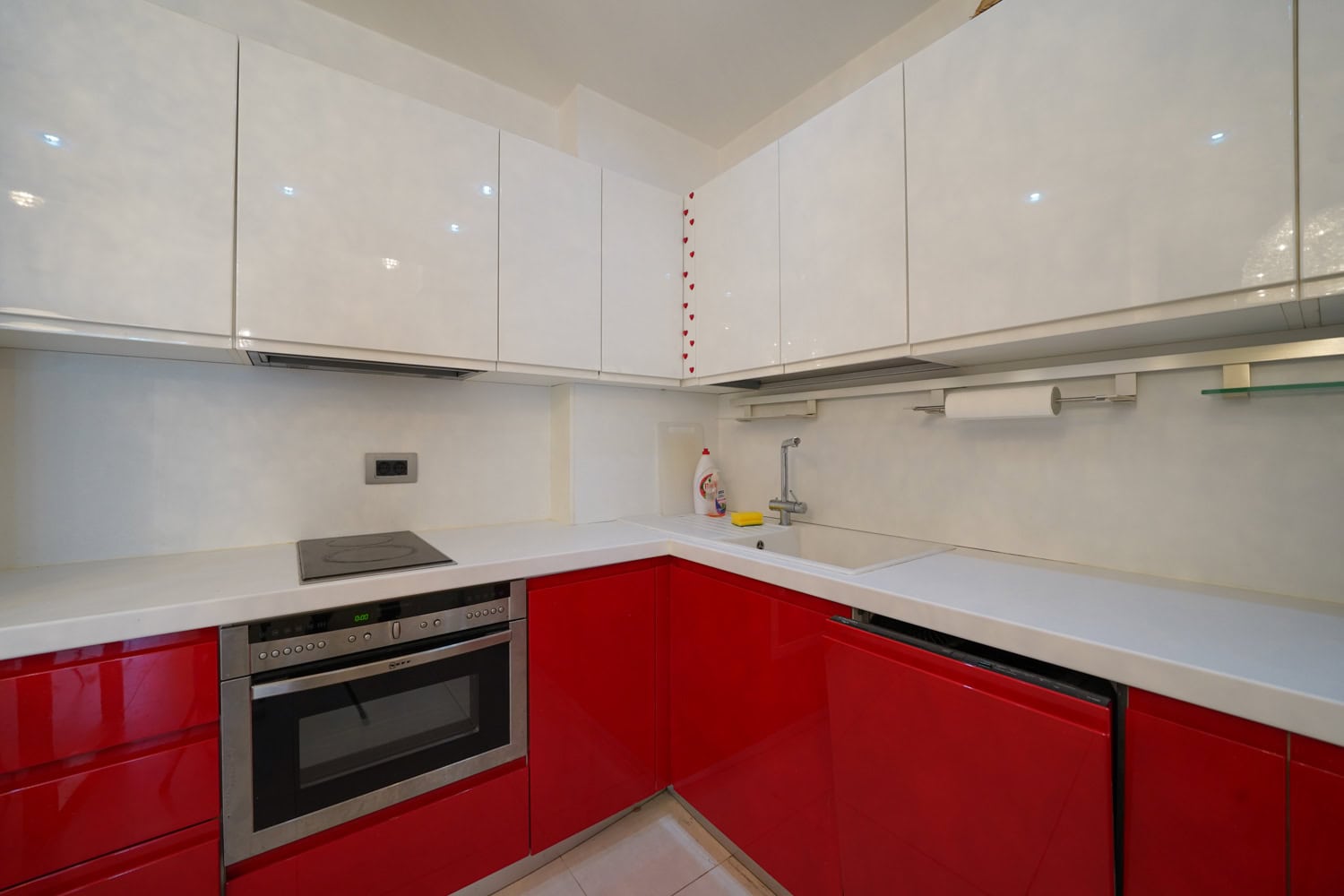 Modern kitchen with red and white cabinets in an apartment in Budva, Montenegro: built-in appliances and a light countertop.