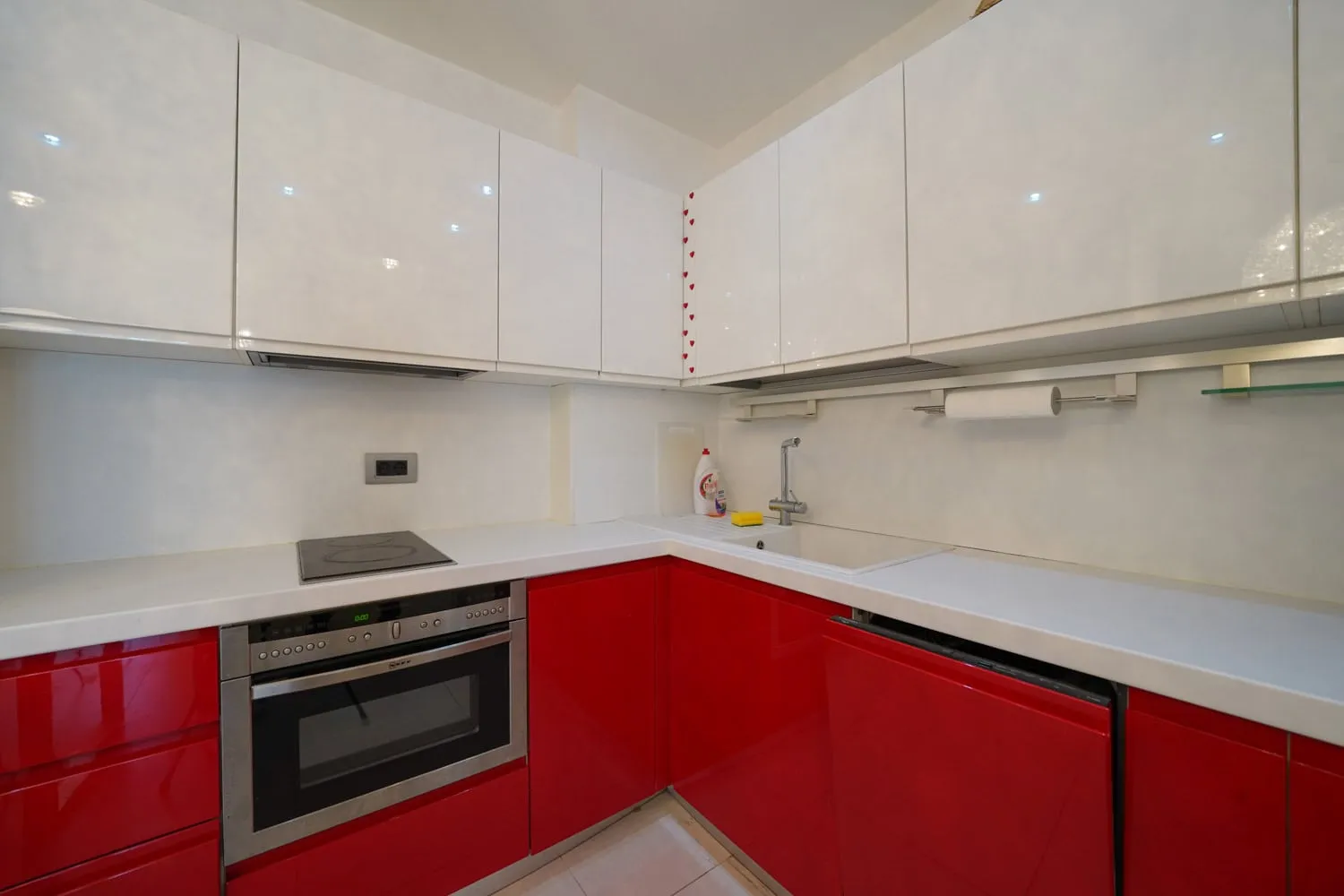 Kitchen with glossy red lower cabinets, white upper cabinets, built-in oven, stove, and sink.